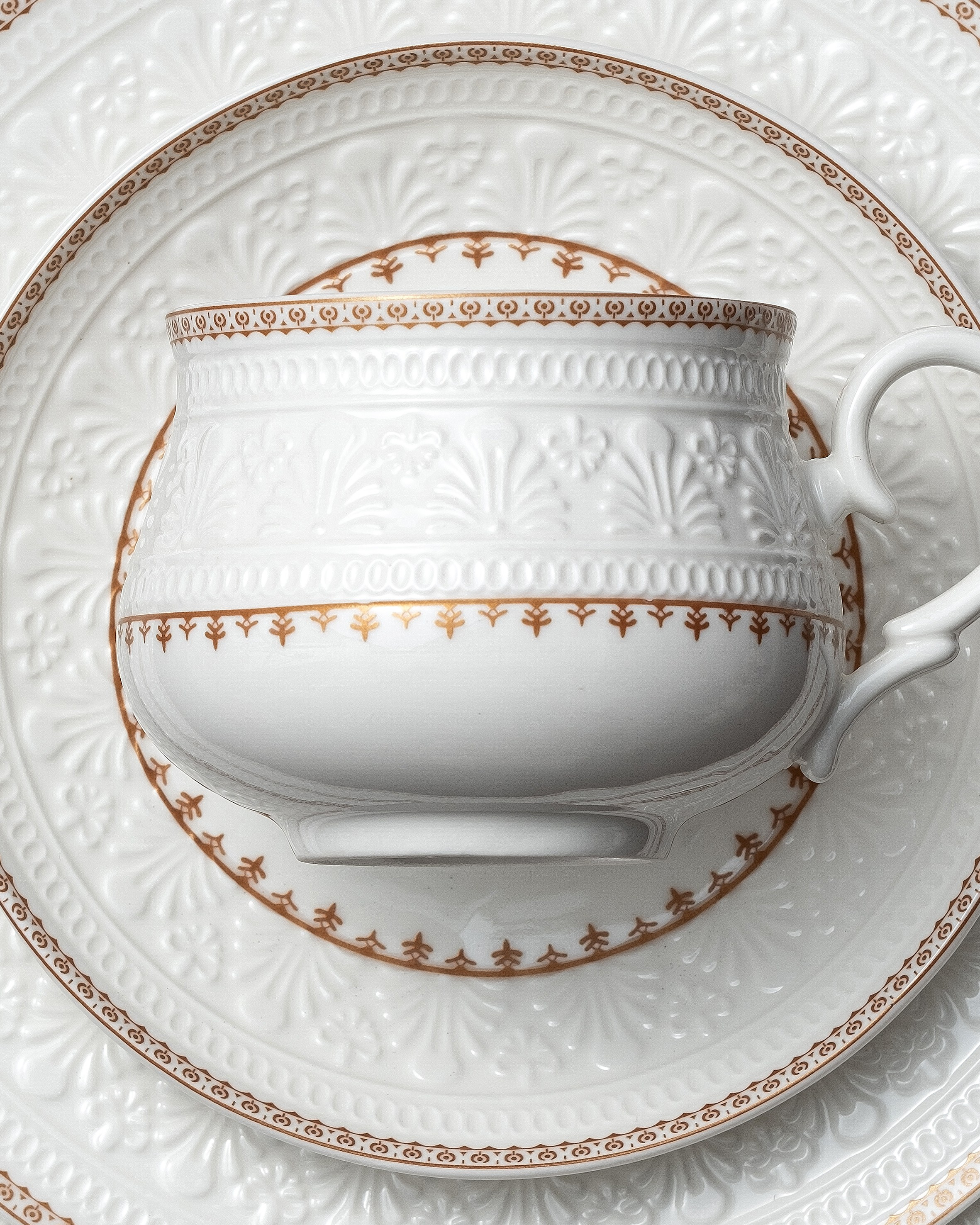 Каталожная фотосъёмка фарфоровой чашки и тарелок с рельефным орнаментом и золотым декором, крупный план деталей, для интернет-магазина и презентаций бренда.