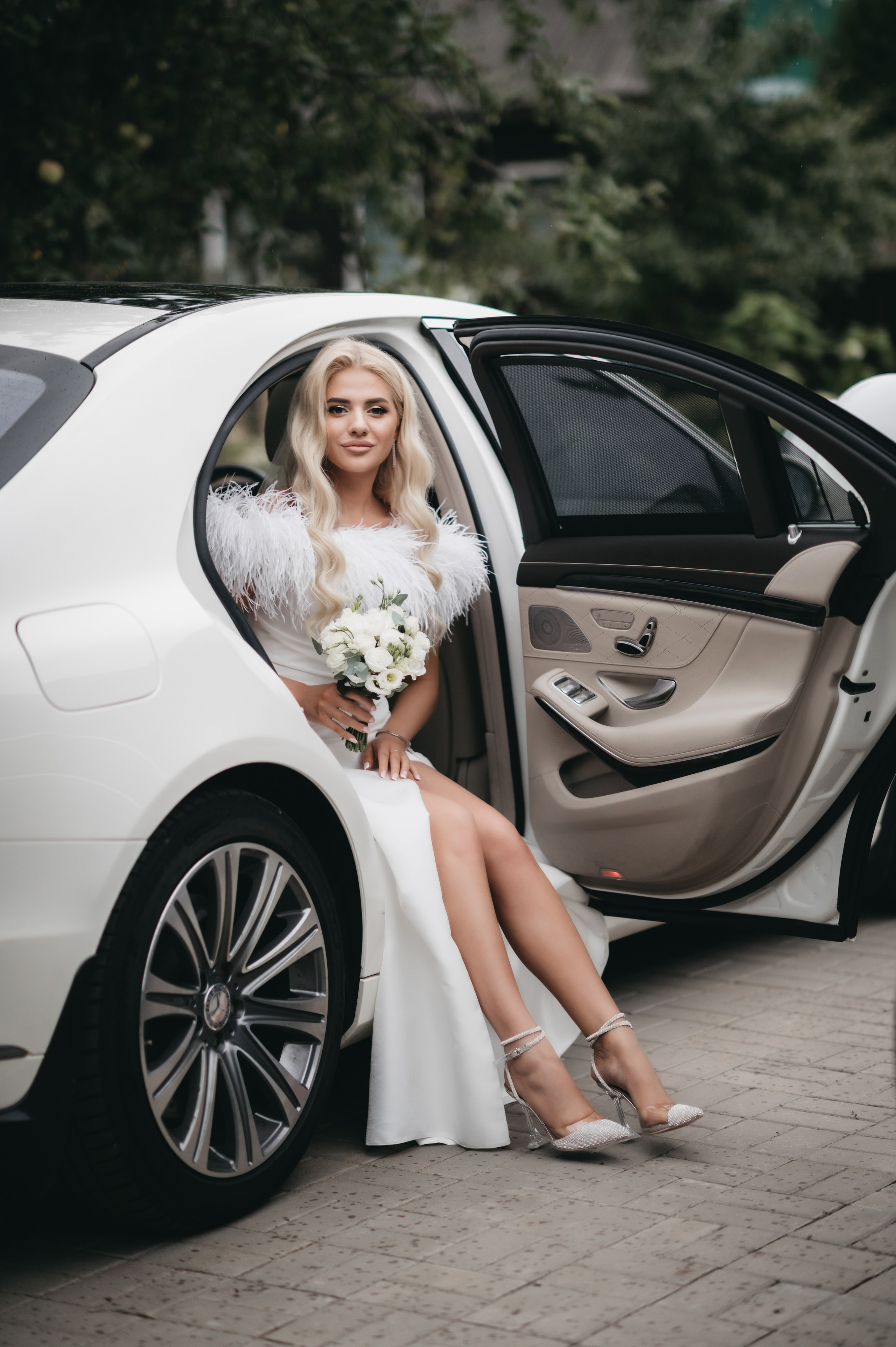 Невеста в свадебном платье и с букетом в белом автомобиле