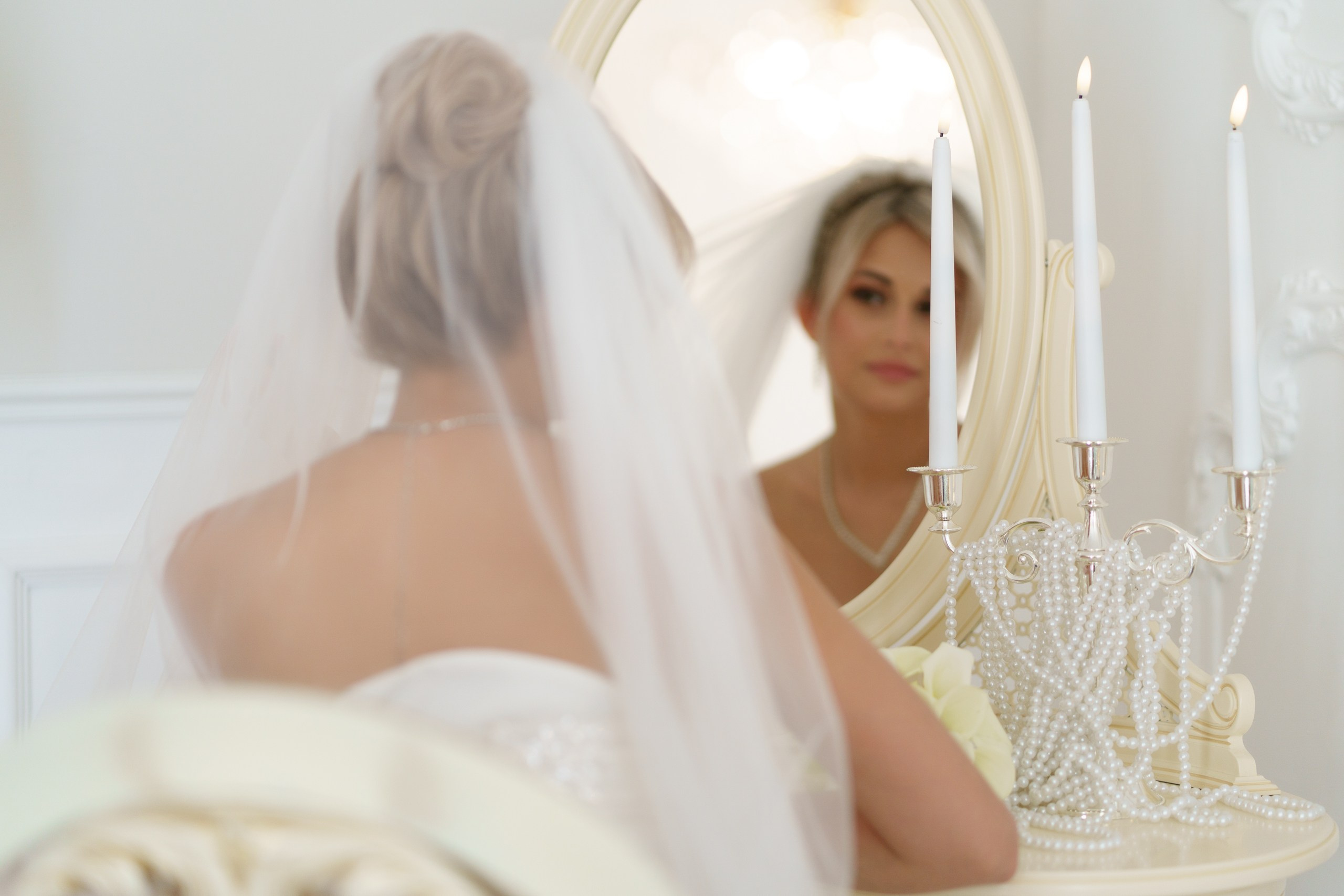 Крупный план невесты в свадебном образе: фата, причёска, отражение в зеркале. Детали композиции — свечи и украшения из жемчуга на столике | свадебный фотограф Екатеринбург