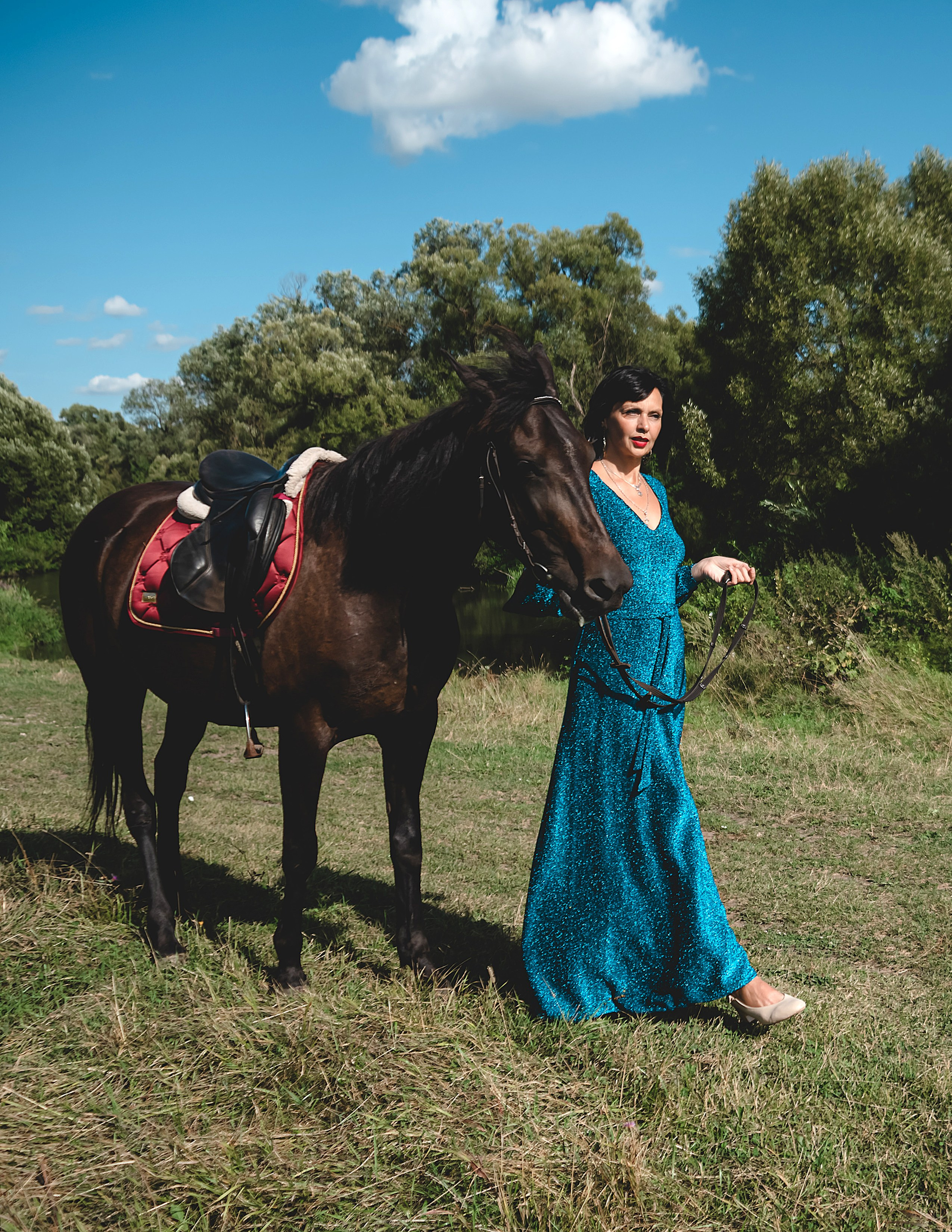 На фото женщина в зеленом платье идет рядом с лошадью.