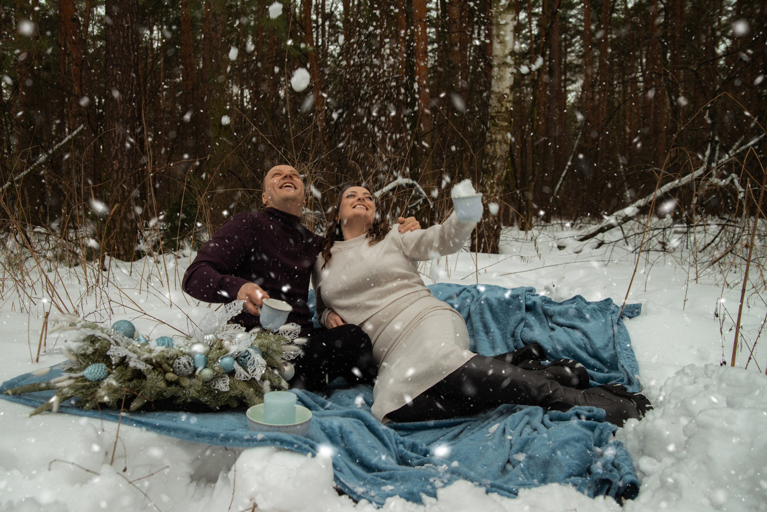 Зимняя фотосессия в лесу влюбленной пары лежащей на снегу и подбрасывающий снег вверх