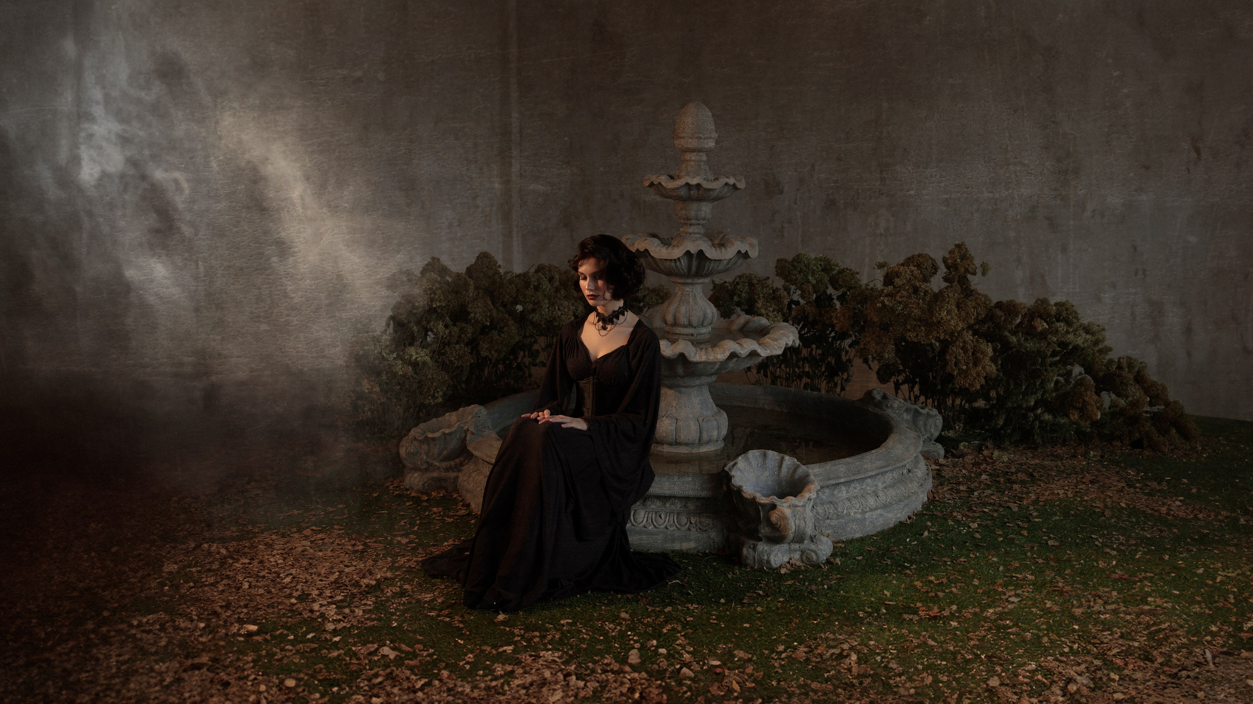 Девушка сидит на краю фонтана, руки сложены на коленях, глаза закрыты, слева идёт дым