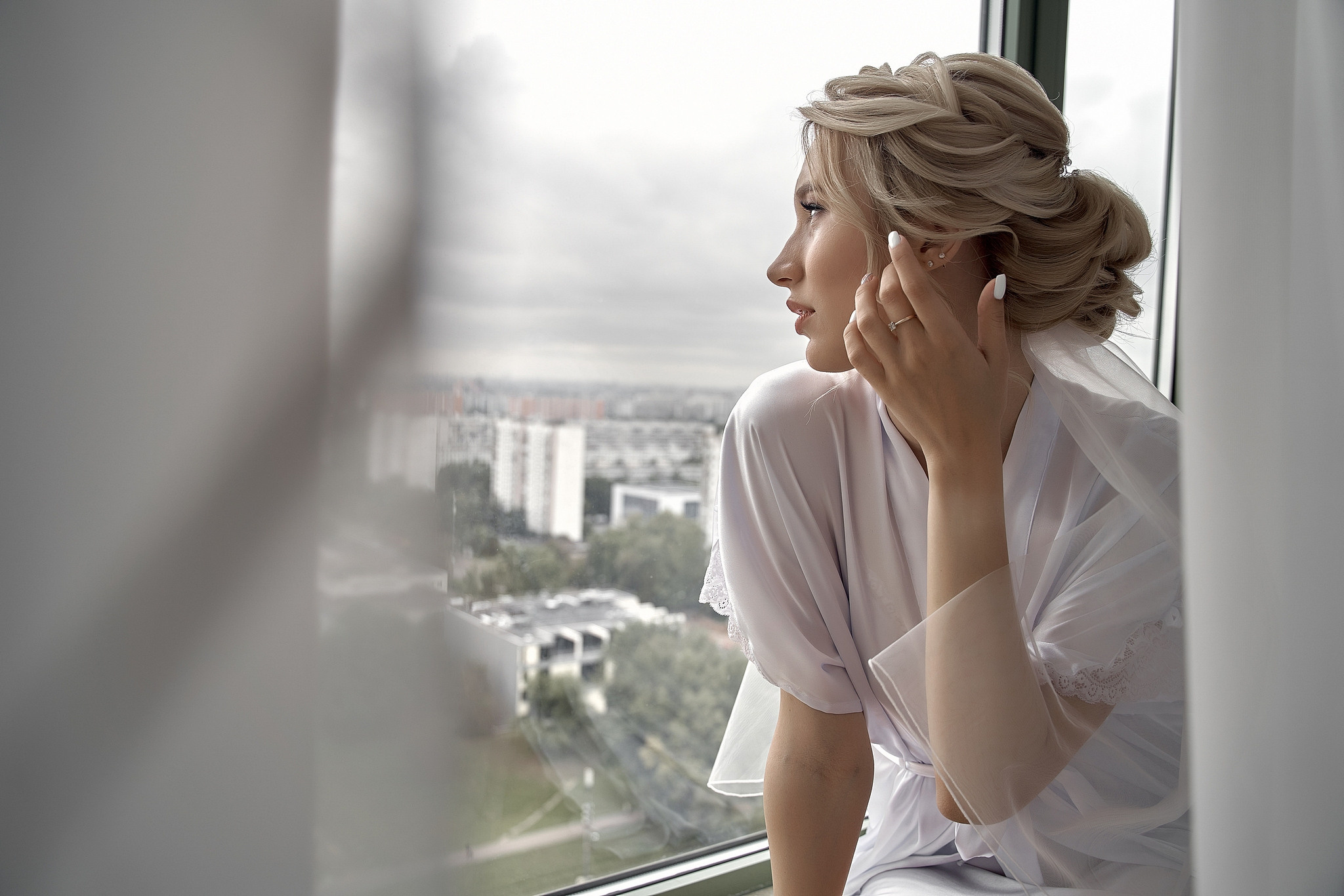 Невеста сидит на подоконнике и смотрит в окно поправляя волосы.Свадебная фотосъемка в  отеле Милан. Свадебный фотограф в Москве  Сергей Гаварос.