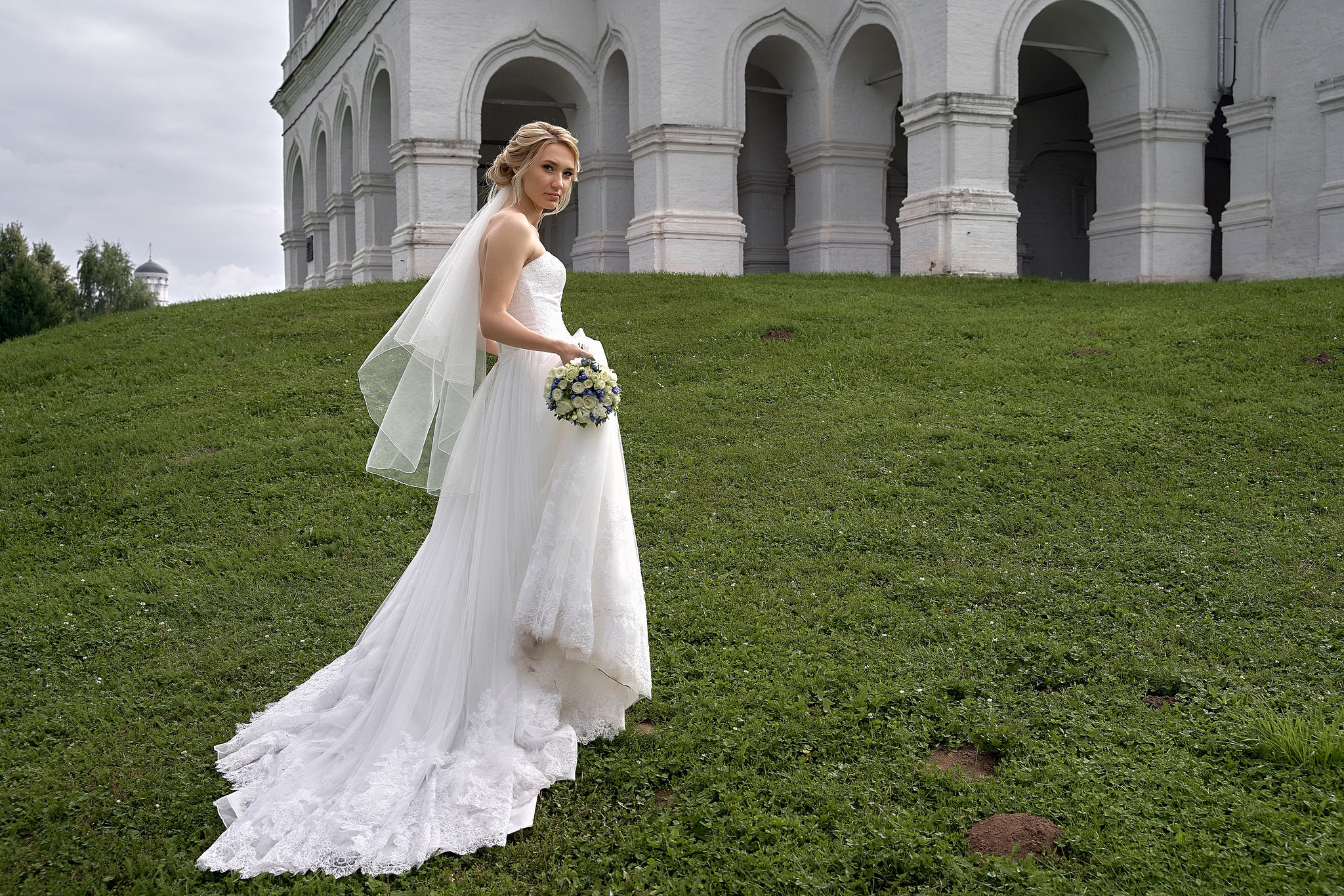 Невеста тдет по зеленой лужайке на колонн.  Свадебная фотосъемка в  Коломенском. Свадебный фотограф в Москве  Сергей Гаварос.