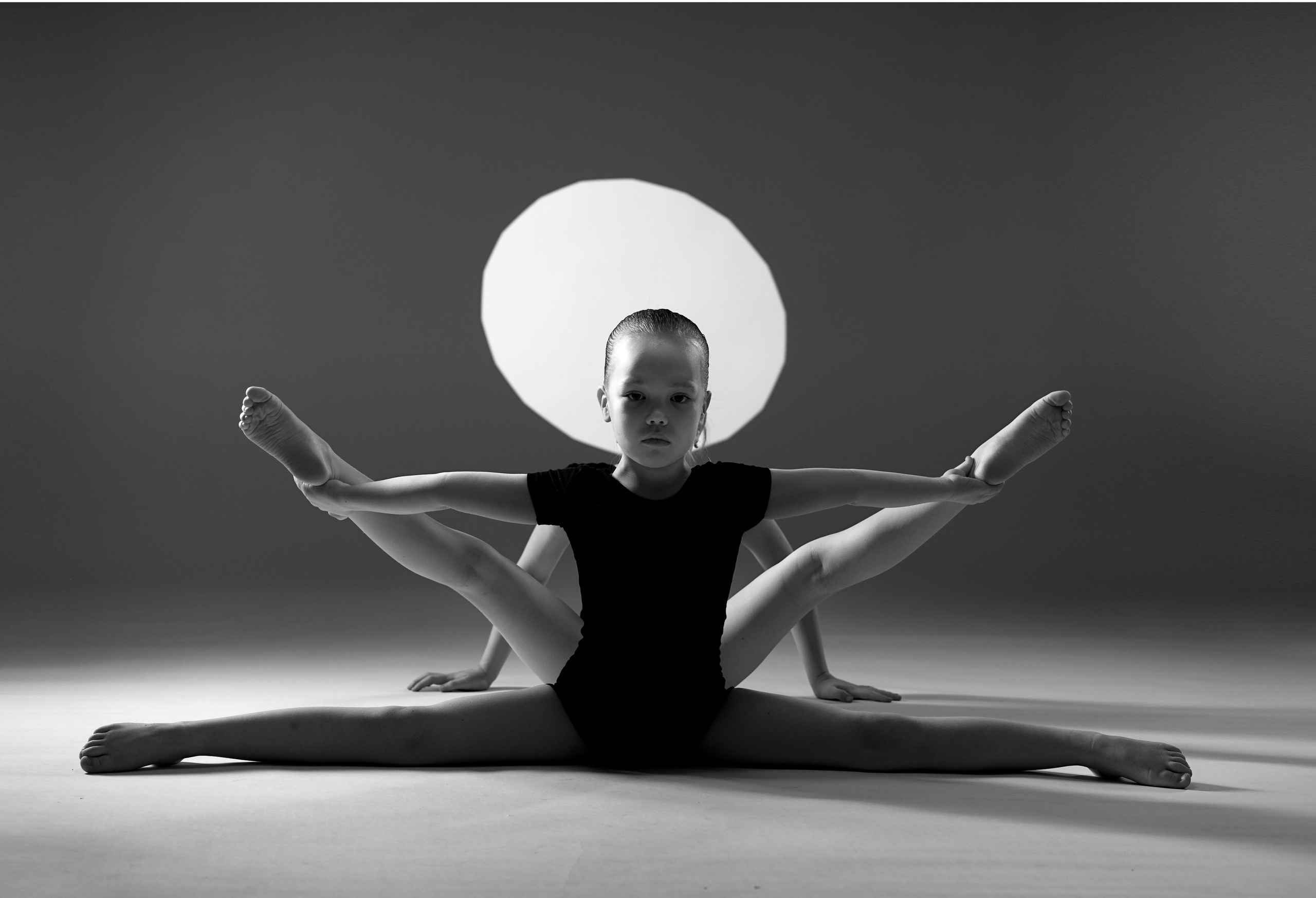 Симметричная арт-композиция с двумя гимнастками на фоне светящегося круга. Черно-белая фотография, подчеркивающая графичность поз и линий тела.