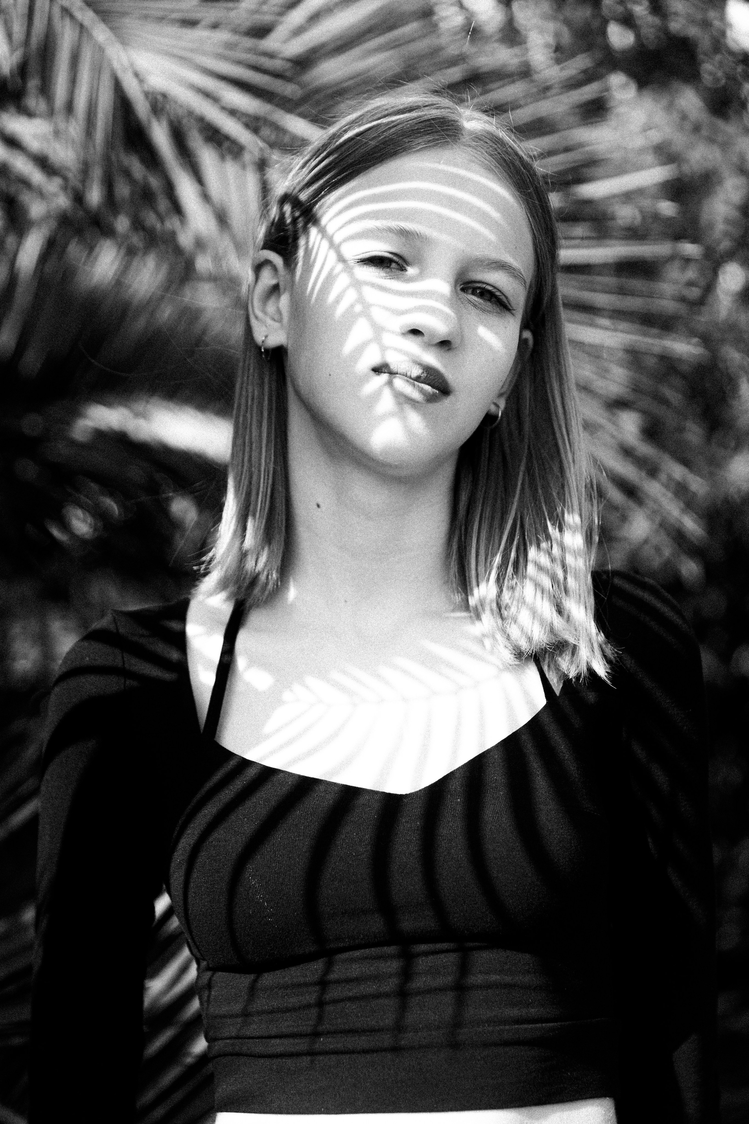 Чёрно-белая фотография на которой девочка освещена полосатые тенью от пальмы