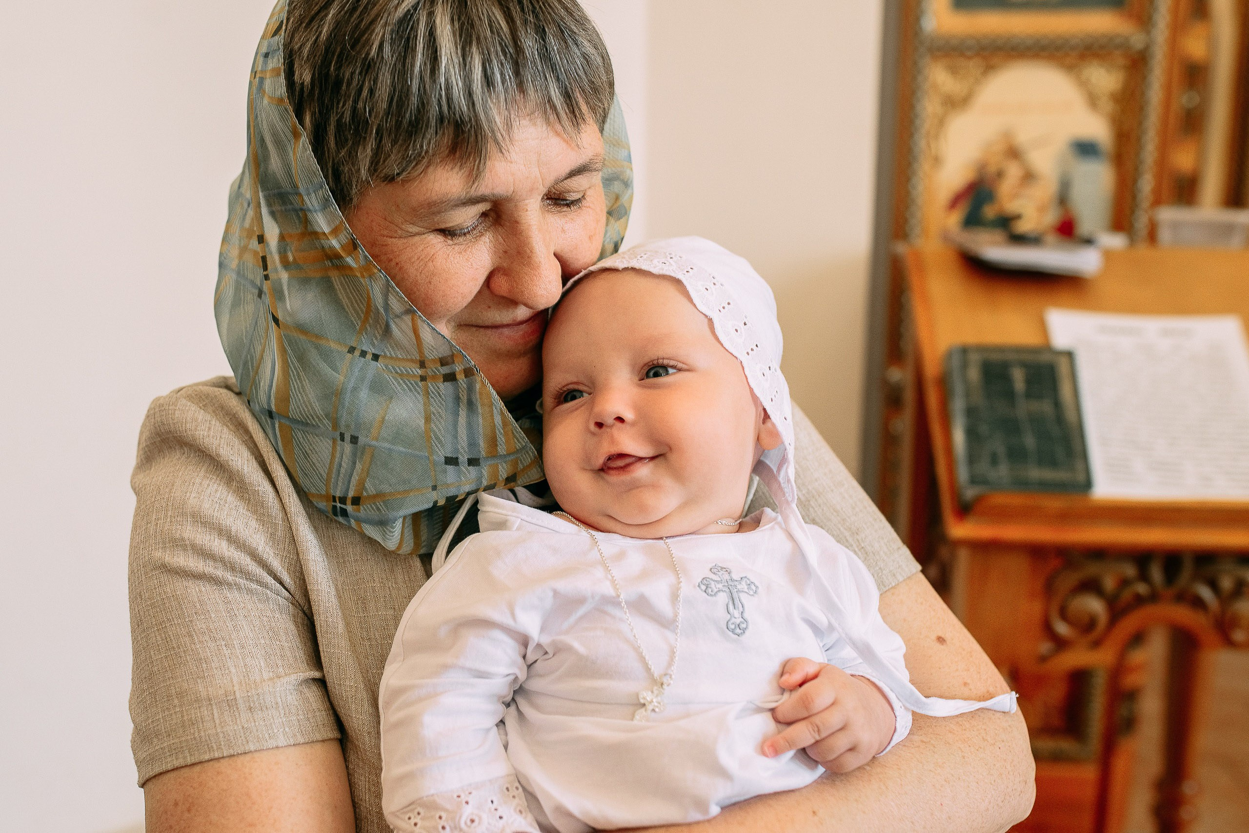 Крупный план: счастливый младенец с нательным крестиком на руках у бабушки во время обряда.