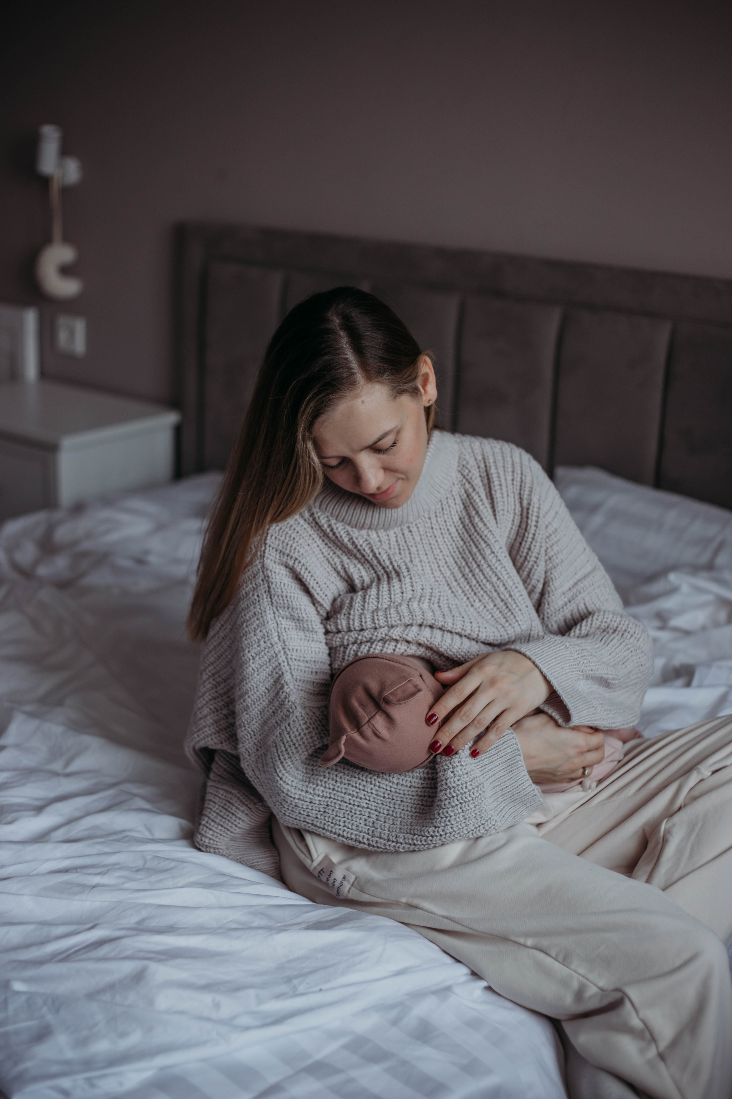 мама сидя на кровати кормит новорожденного малыша на руках