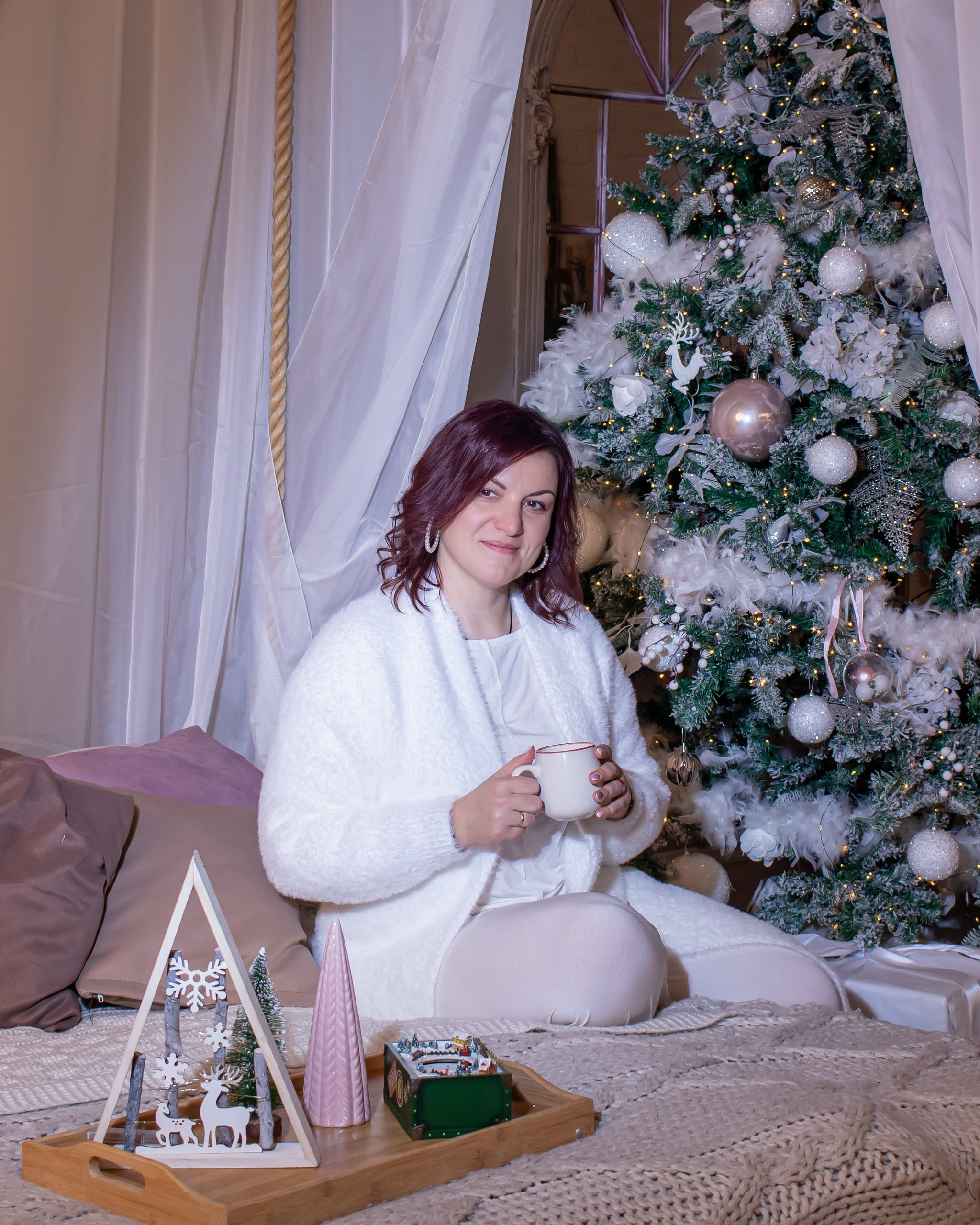 Молодая женщина позирует рядом с новогодней ёлкой в светлой студии, фотограф Карасёва Елена