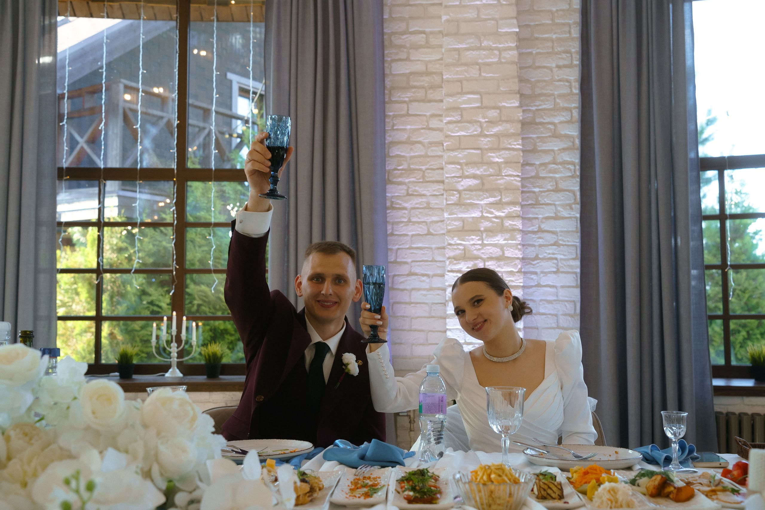 Жених и невеста за столом поднимают бокалы — тост на свадьбе
