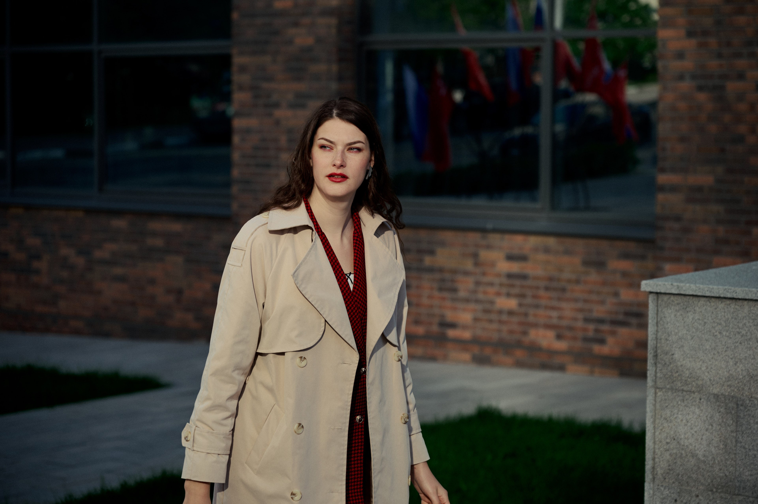 Городской портрет: женщина в деловом образе стоит у бетонной стены, отражающей флаги — акцент на уверенности.