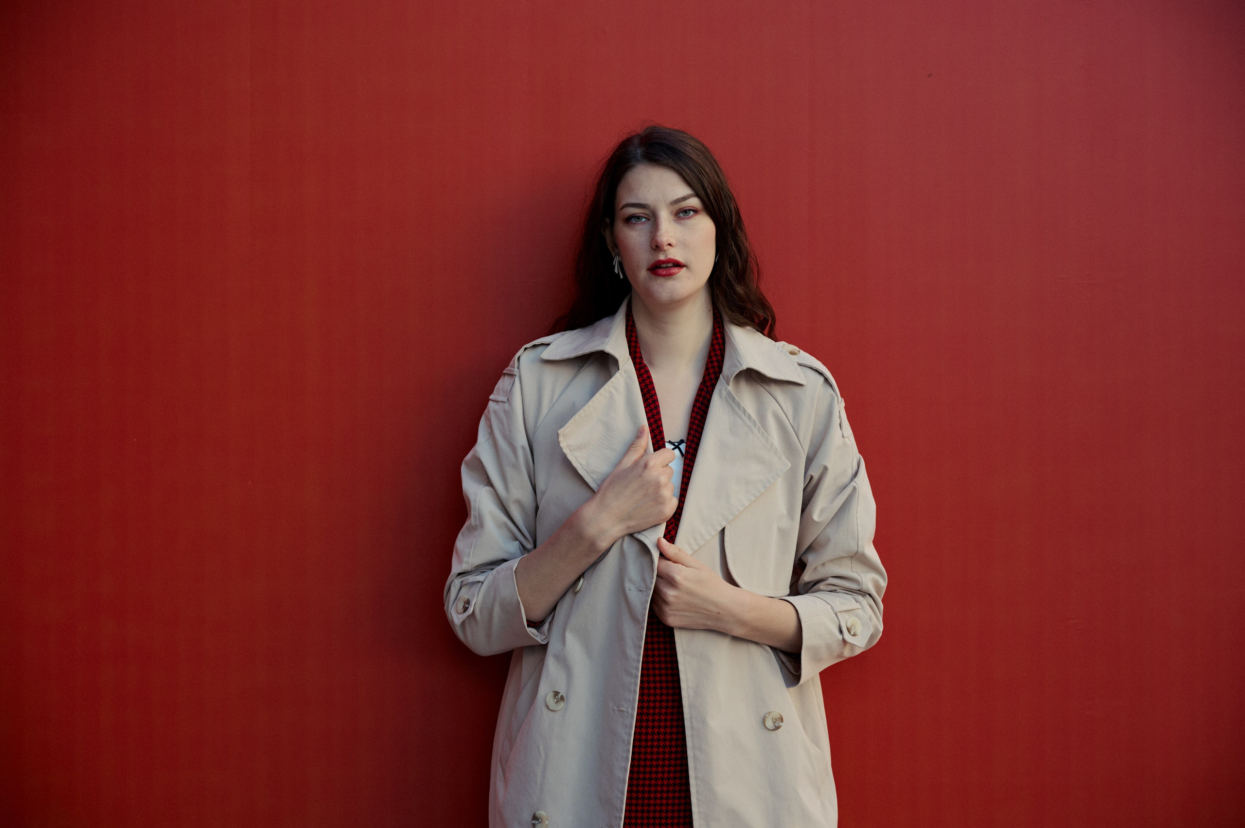 Фотосессия в студии с красным фоном — строгий портрет в пальто, руки скрещены, минималистичный стиль.