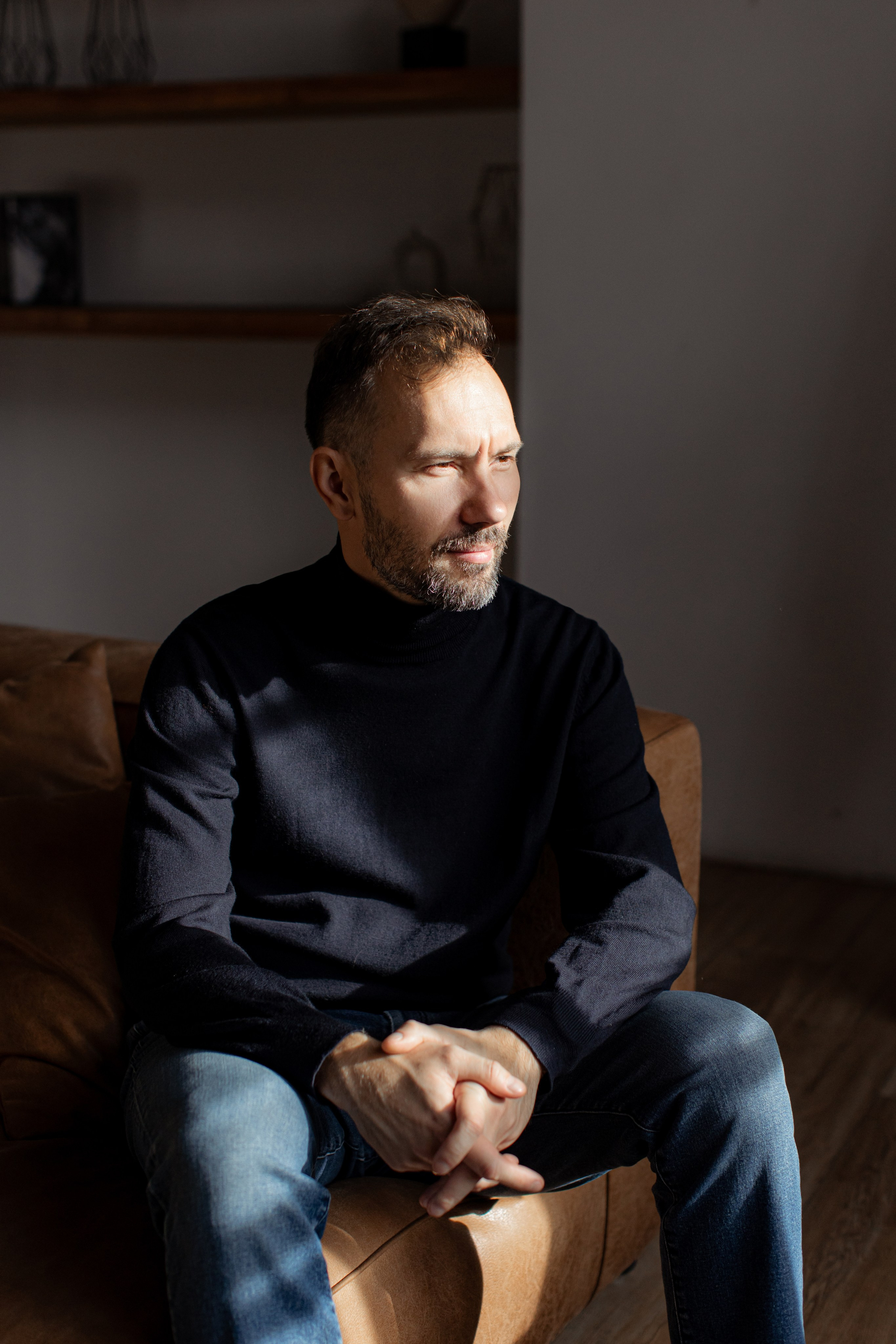 Деловой мужчина в водолазке и синих джинсах сидит на кожаном диване