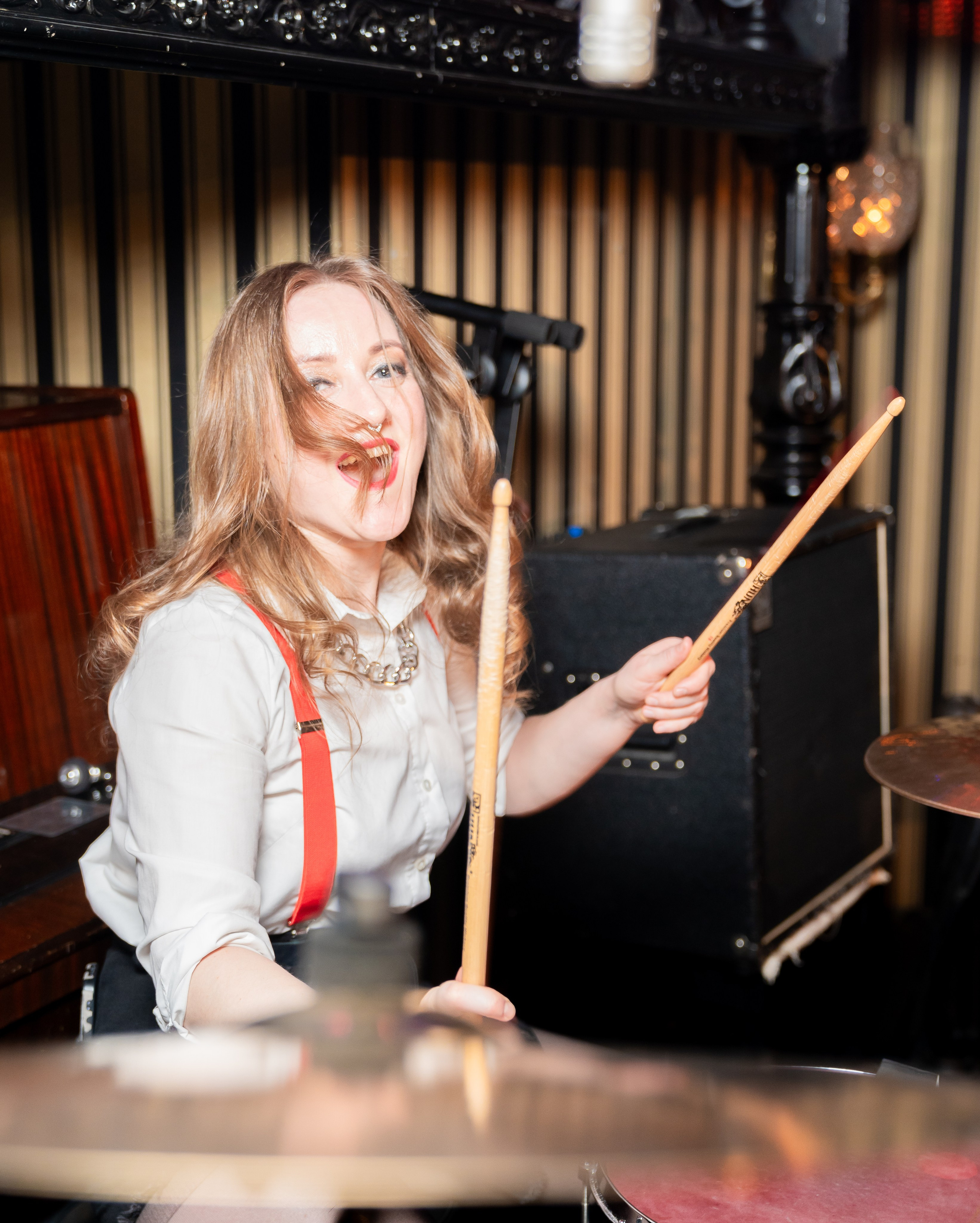 Бар Дуглас. Энергичная девушка-барабанщица с длинными волосами и красными подтяжками играет на ударной установке. Яркая портретная фотография музыканта. Автор: Евгений Мальцев (evrednix.ru).