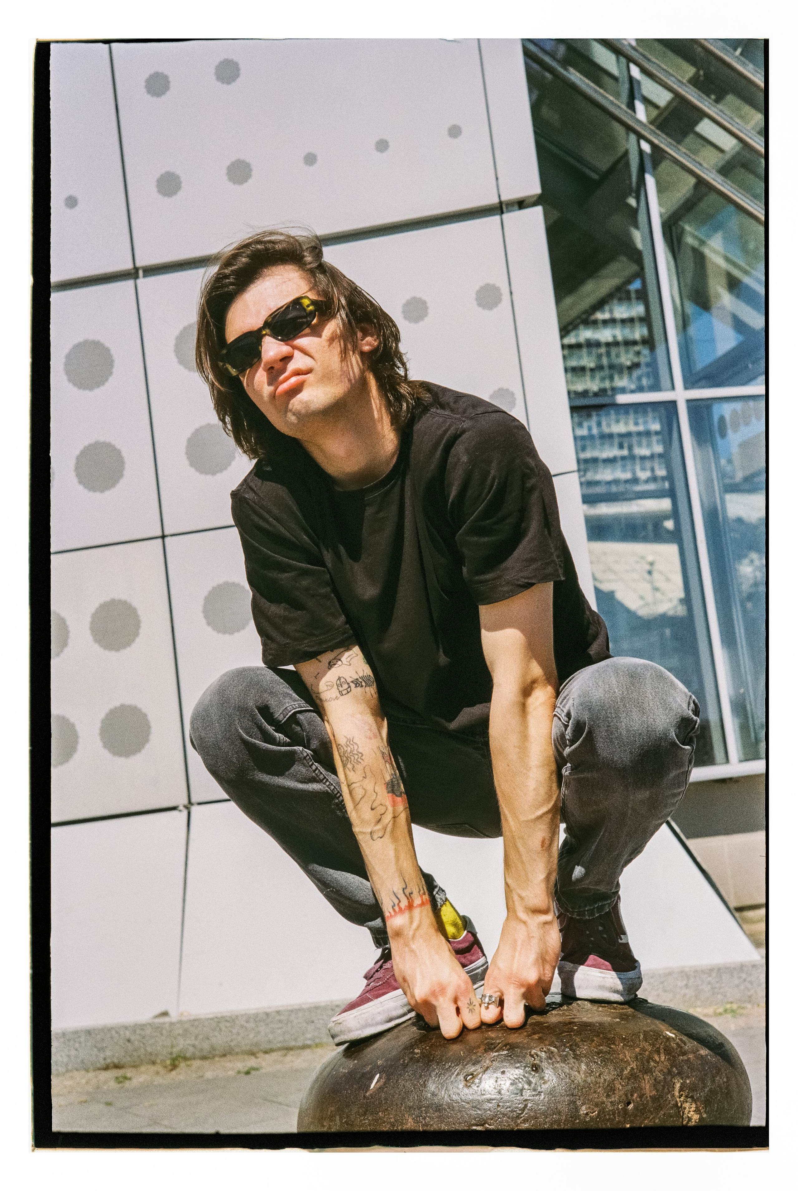 Фотография парня с длинными волосами, в полуприсяди на металлической тумбе