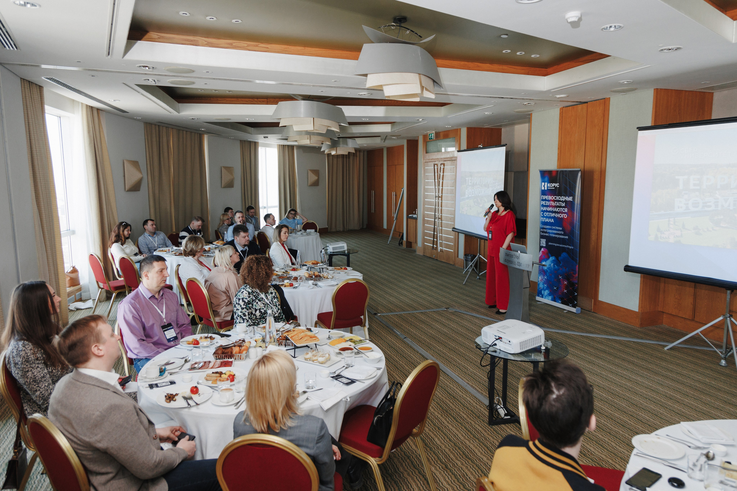 Репортажный кадр с бизнес-завтрака: ведущий представляет новый проект перед аудиторией.