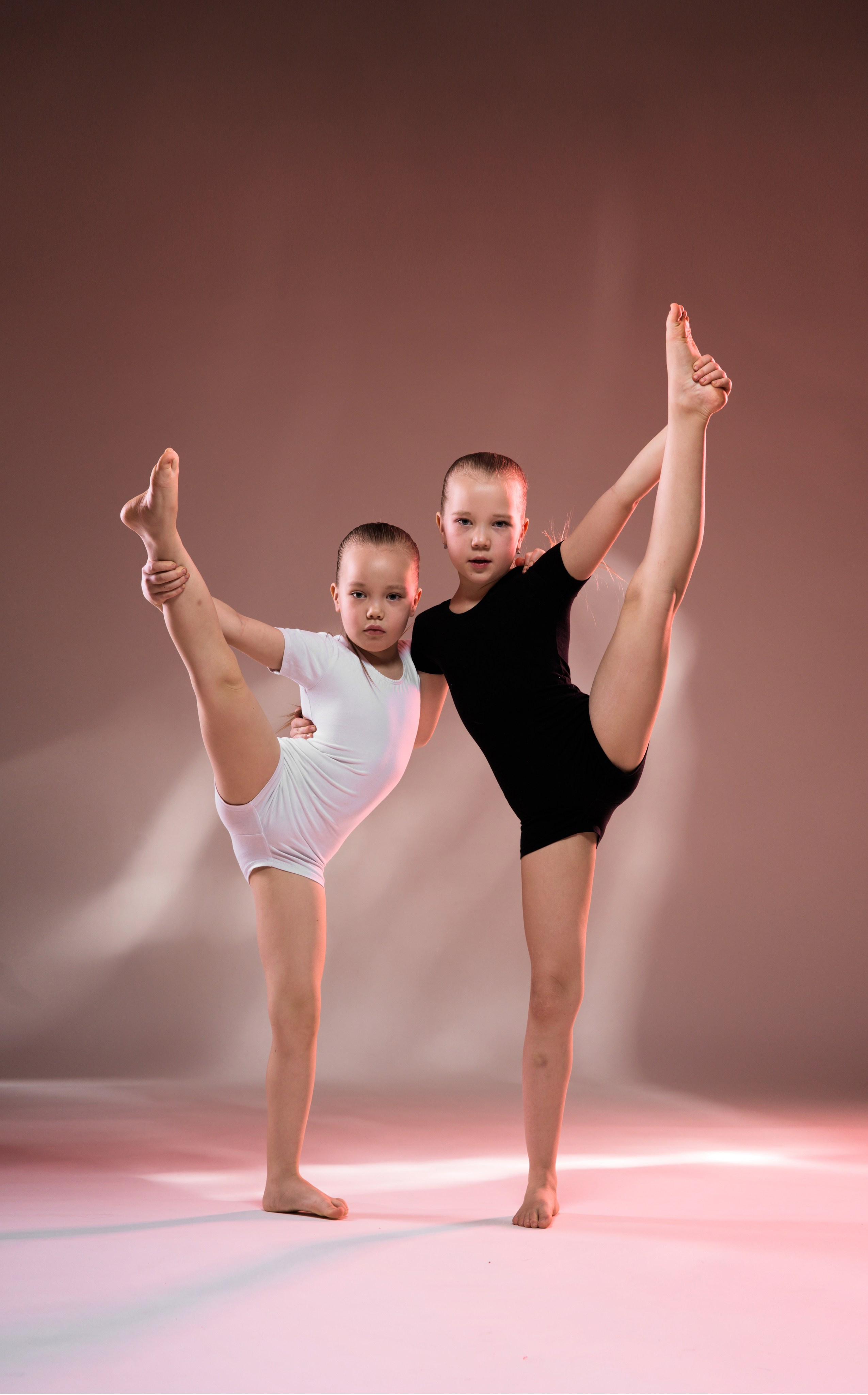 Гимнастки в полный рост на светлом фоне в классических позах. Профессиональная арт-фотография, акцент на чистоту линий и дисциплину.