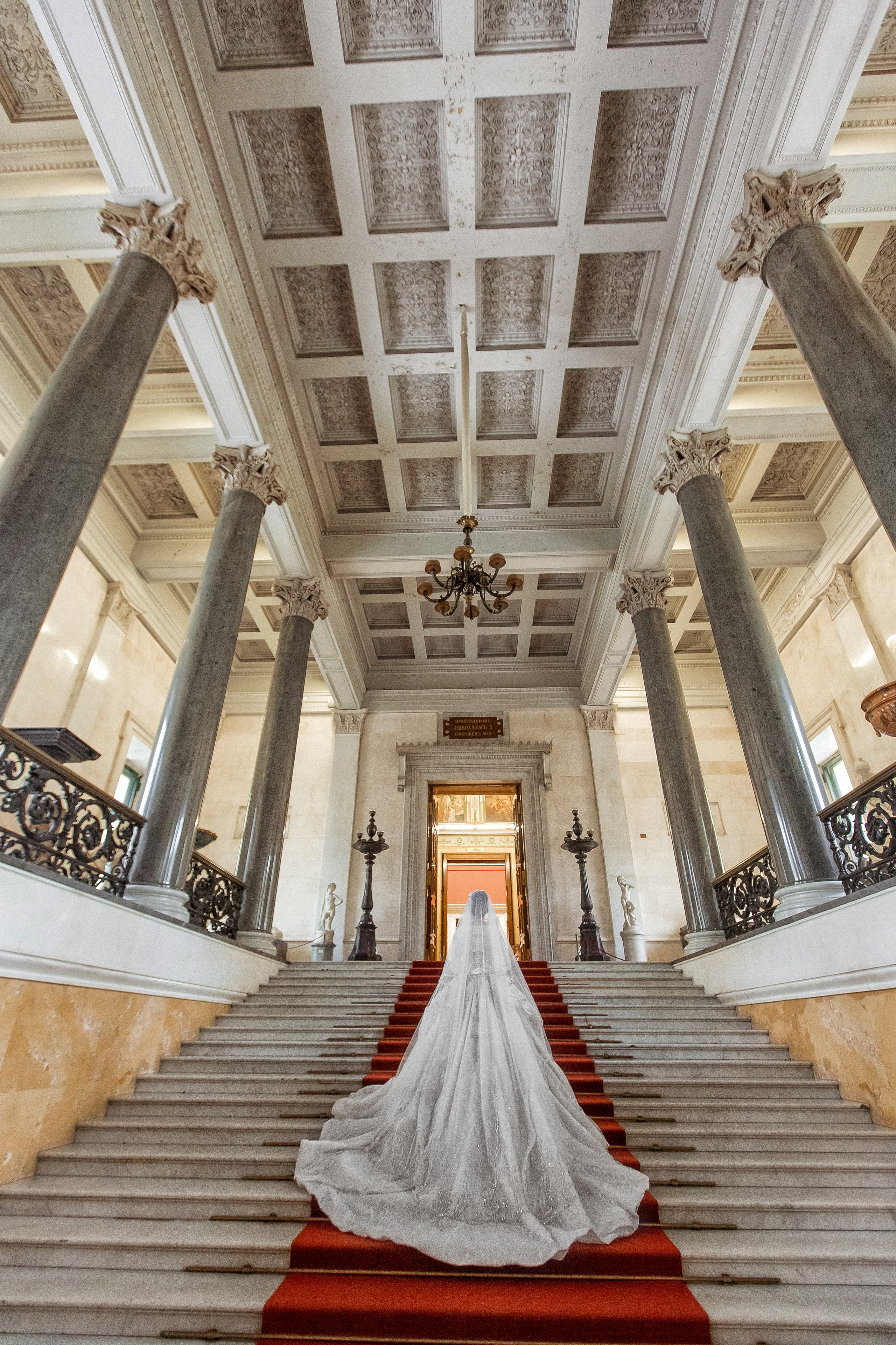 Свадебное платье принцессы на шикарной лестнице с красной ковровой дорожкой и колоннами
