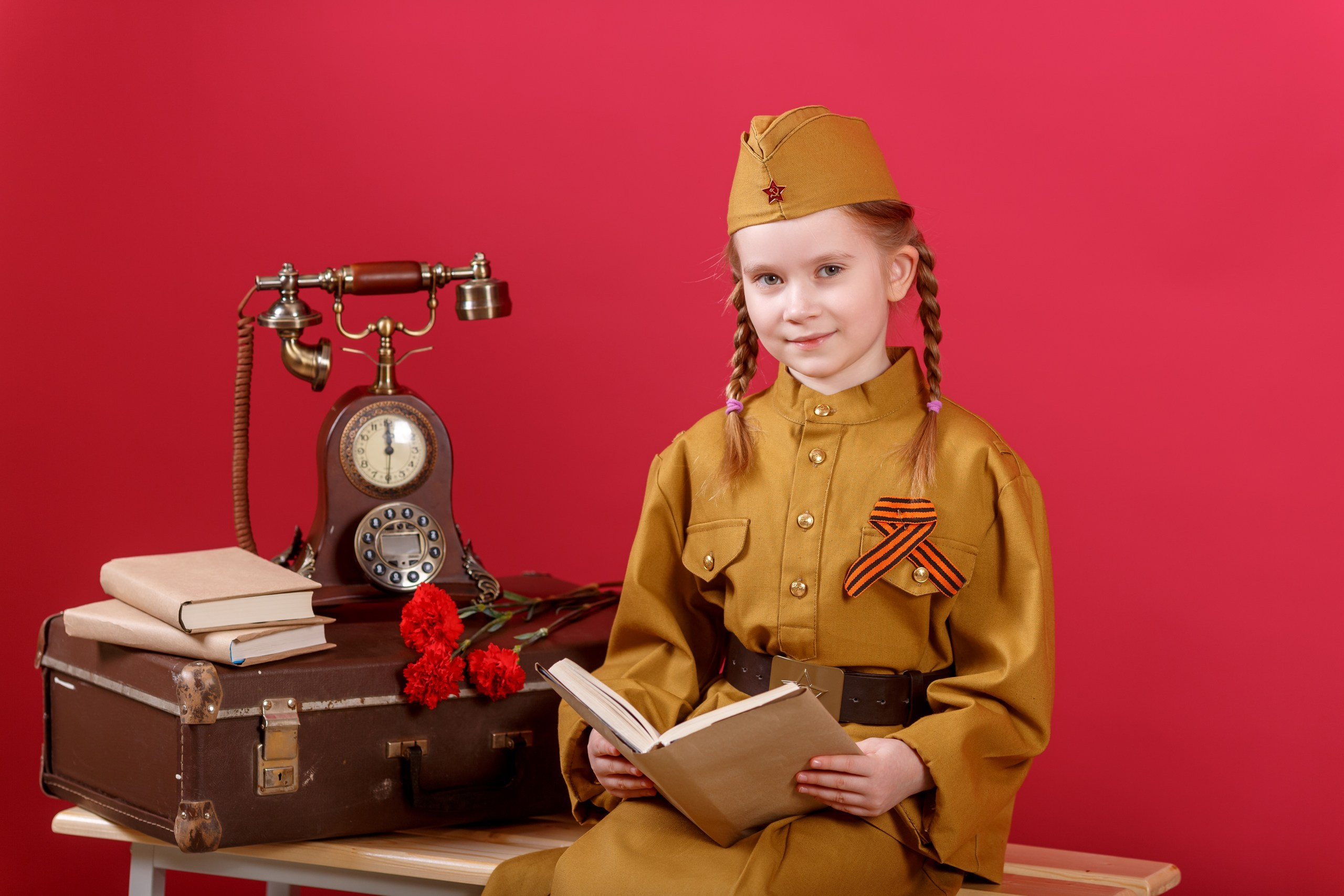Патриотической фотопроект к Празднику Великой Победы.На красном фоне девочка в военной форме с книгой в руках. Работа фотостудии Вышка в Домодедово.