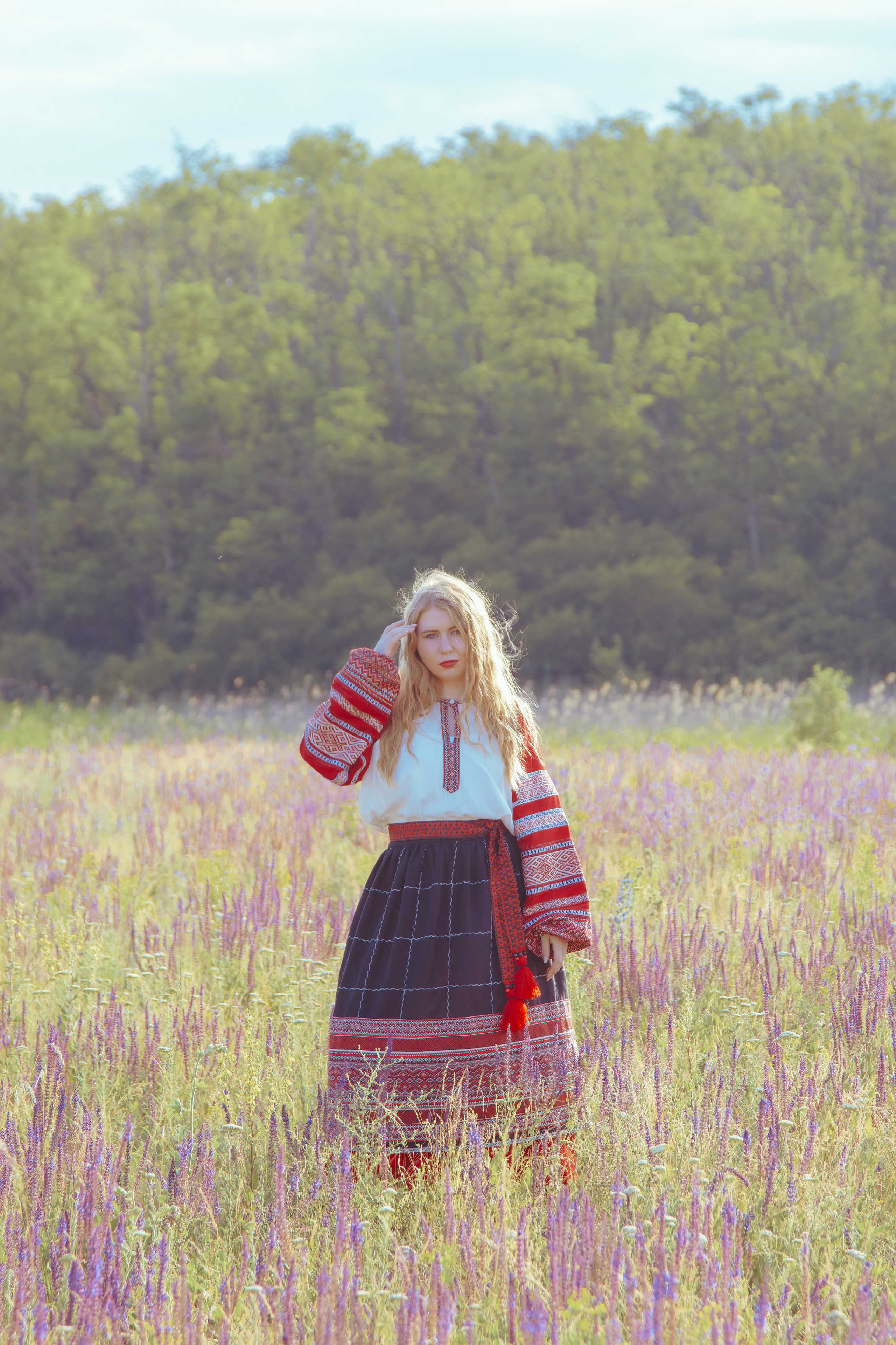 Одинокая девушка стоит в поле поправляя свои волосы