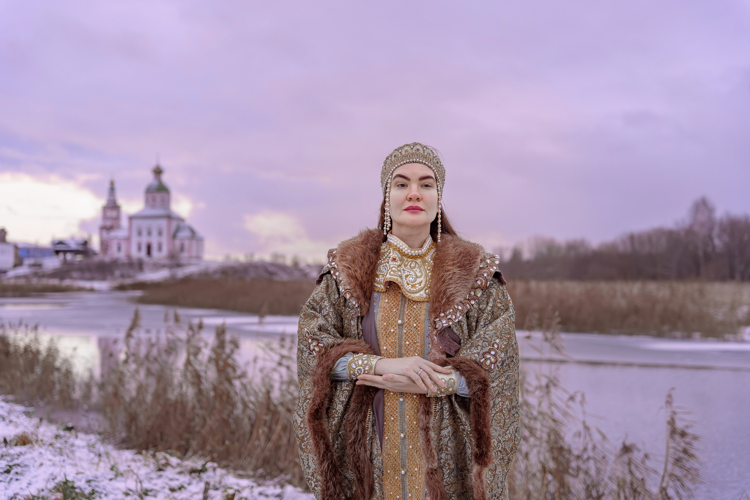 A girl in a boyar costume on the background of a temple in Suzdal by the river