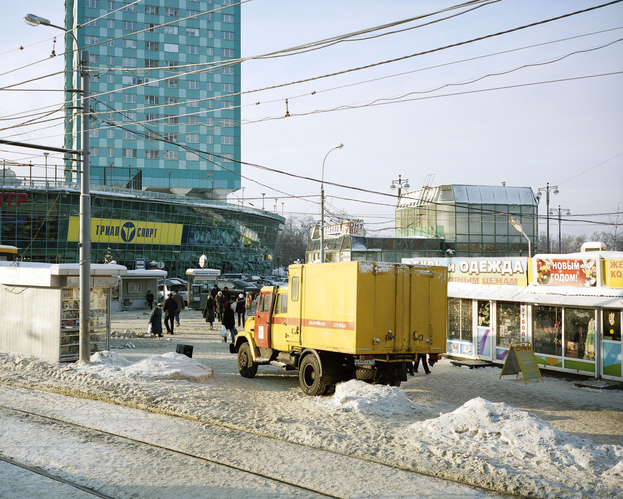 PLATE 40: Residential buildings, shopping mall, assorted semi-permanent shop buildings and kiosks, tram tracks, waste bins, pay kiosk, municipal services truck, assorted shop signs, lamp posts with power lines, A/C units, snow, figures of people