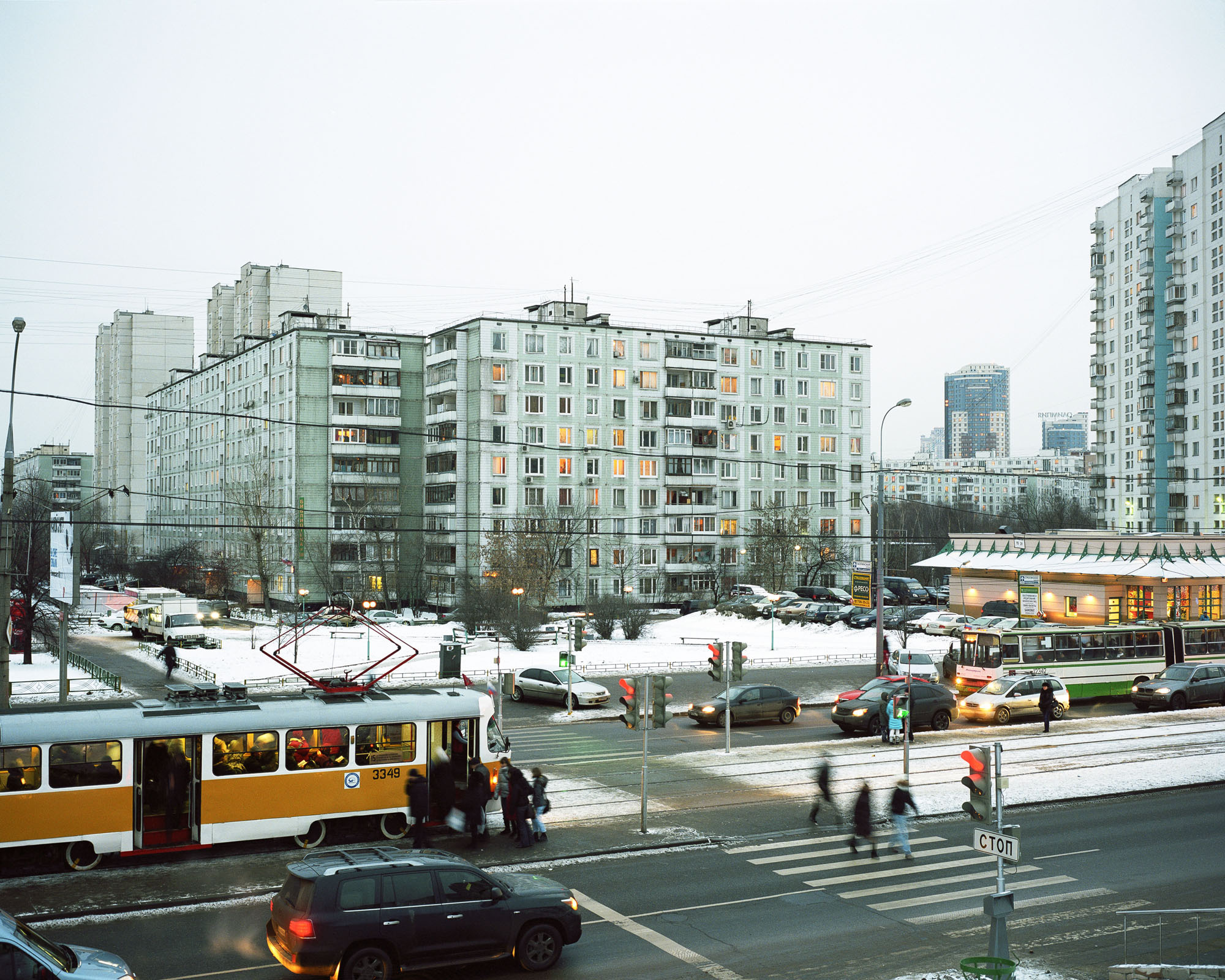 PLATE 58: Residential buildings, tram car, bus, traffic lights, pedestrian crossing, tram tracks, cars, road signs, assorted signs and billboards, benches, shop vans, single-storey café building, figures of people, A/C units, lamp posts with power lines, assorted barriers