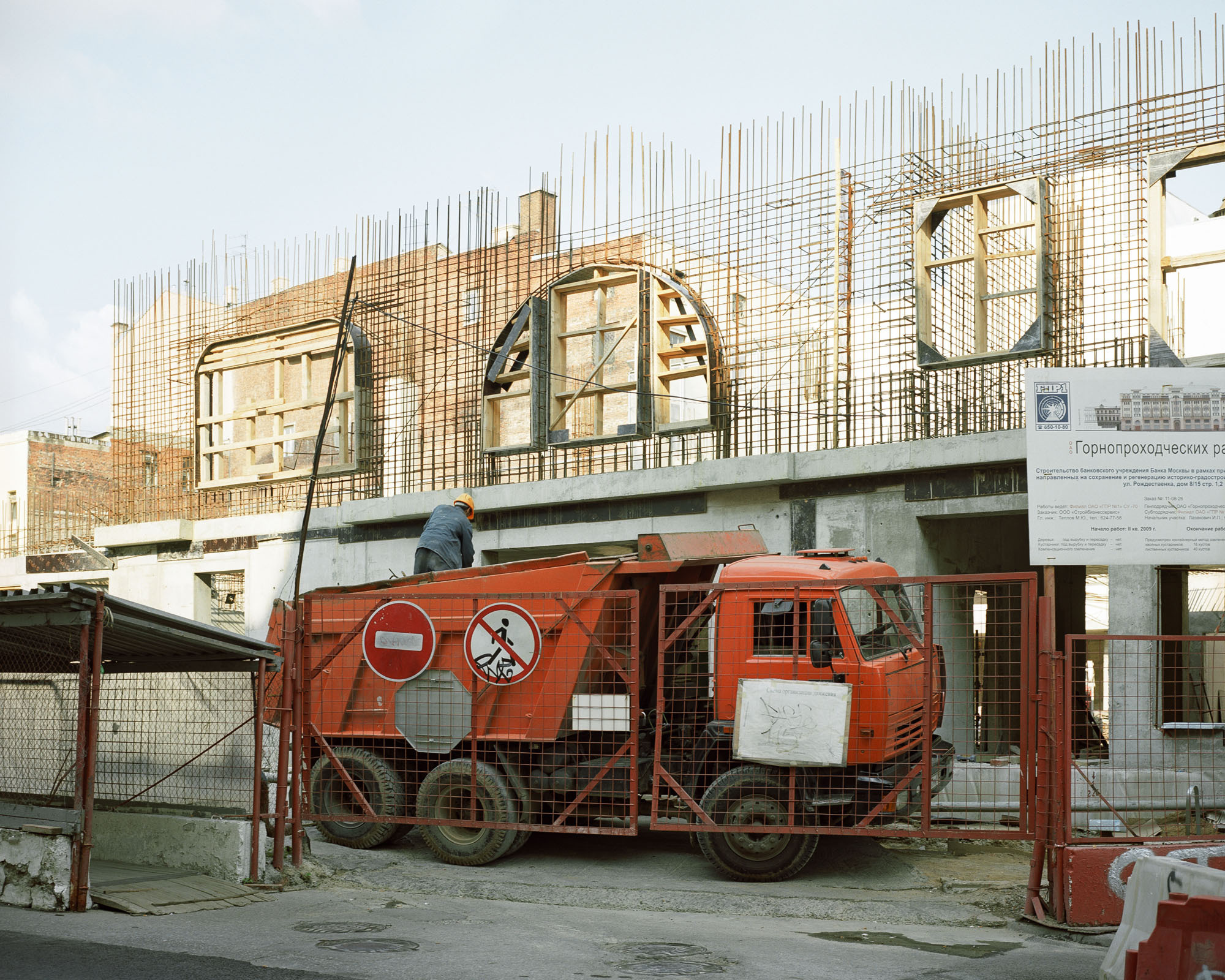 PLATE 53: Concrete foundation c/w rebar cage, dump truck, figure of construction worker, assorted barriers, road signs, notice board, power lines, covered pedestrian walkway