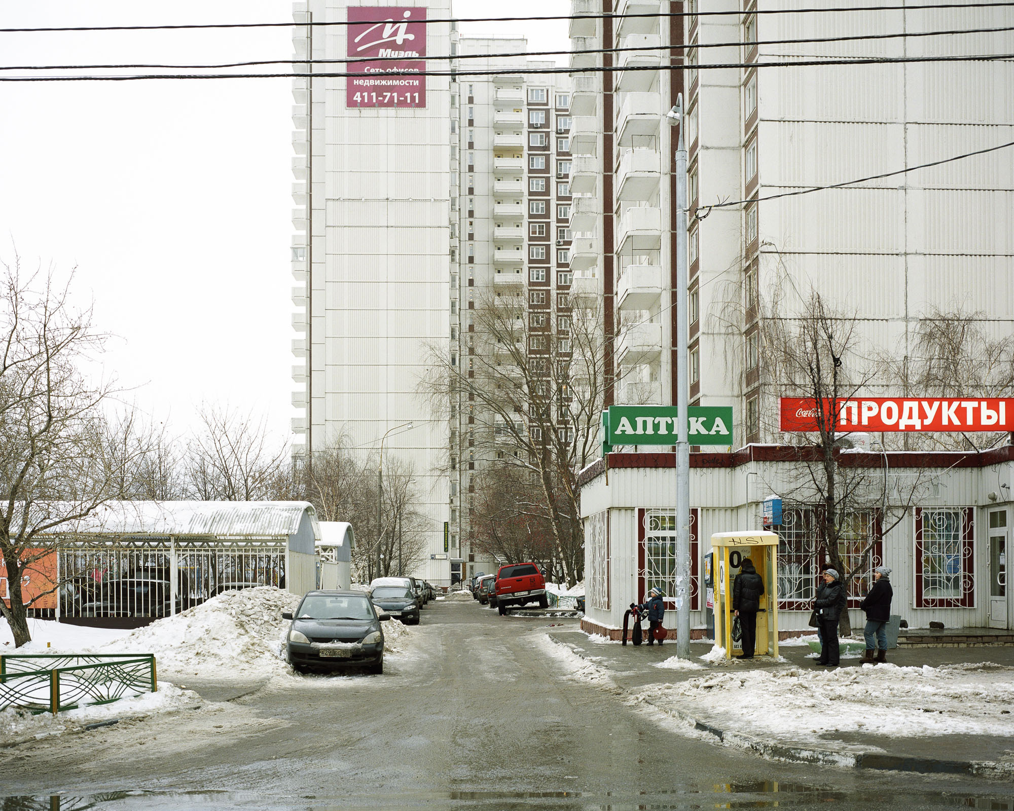 PLATE 21: Residential buildings, semi-permanent shop building c/w ‘Pharmacy’ and ‘Groceries’ signs, payment kiosk, barriers, covered parking (also includes cars, trees, figures of people, A/C units, lamp posts with electrical lines)
