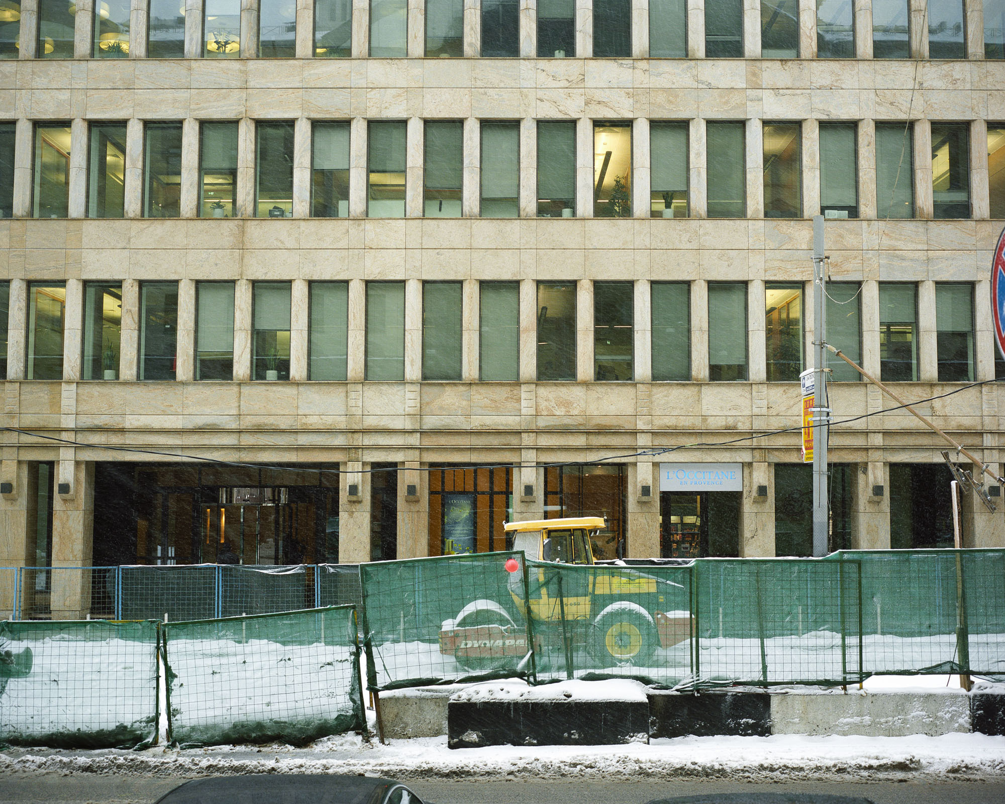 PLATE 7: Office building with furnished interiors, construction barriers (with net and warning light), compactor, concrete blocks, shop signs, lamp post