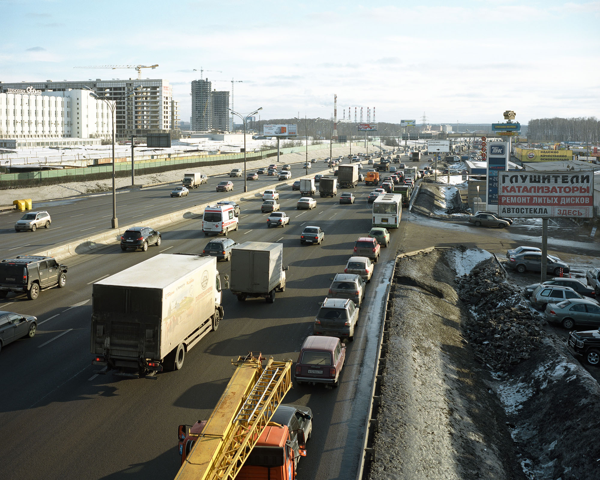 PLATE 26: Multi-lane freeway (with guardrails and drainage channel), billboards and banners, signage, lamp posts, assorted vehicles, filling station, parking space, office buildings, construction cranes (also includes chimneys, trees, pedestrian bridge)
