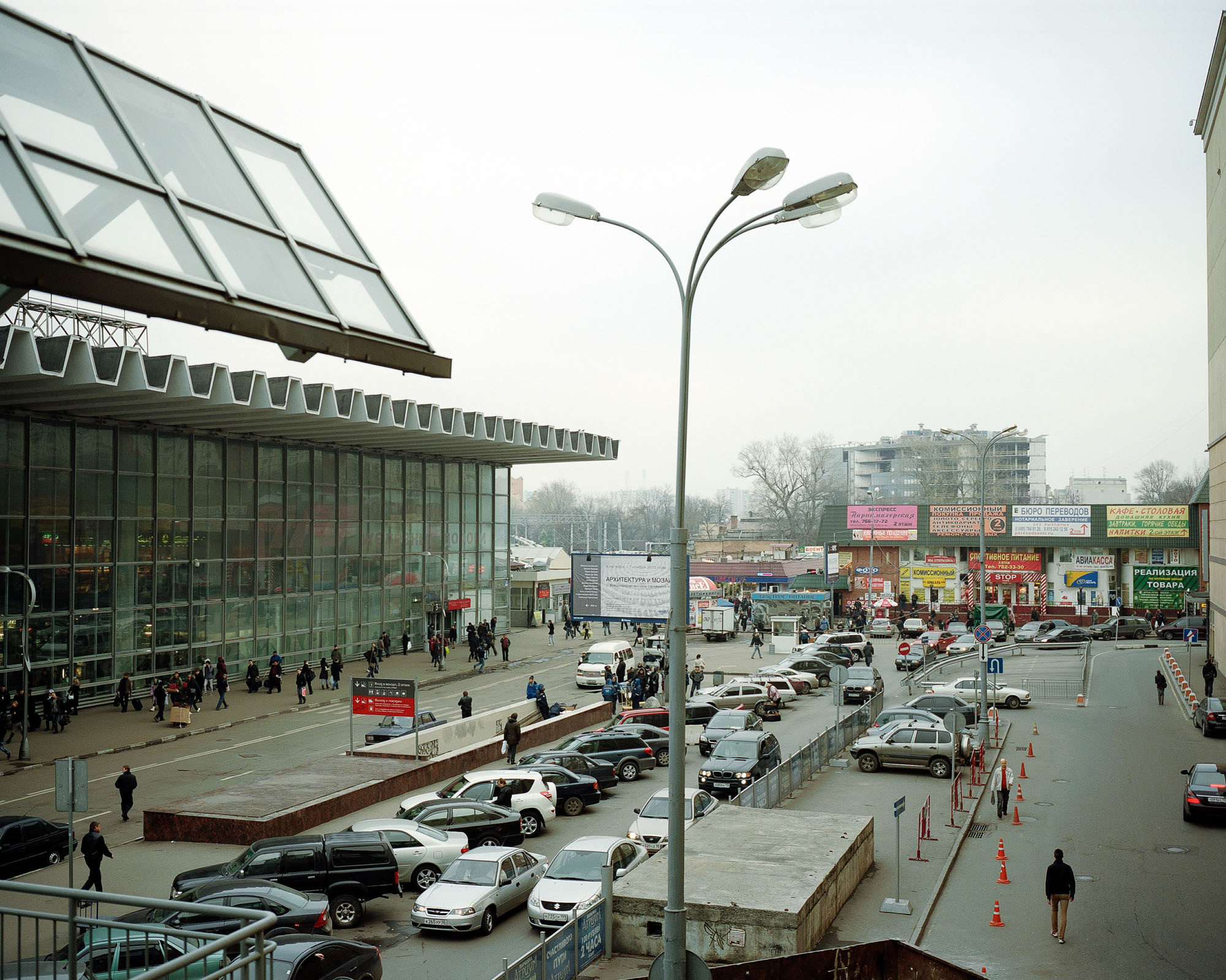 PLATE 59: Glass façade building, parking space, subway passage exit, kiosks and shops, permanent and temporary barriers, lamp post, billboards and signage (also includes cars, A/C units, road signs, figures of people, trees)
