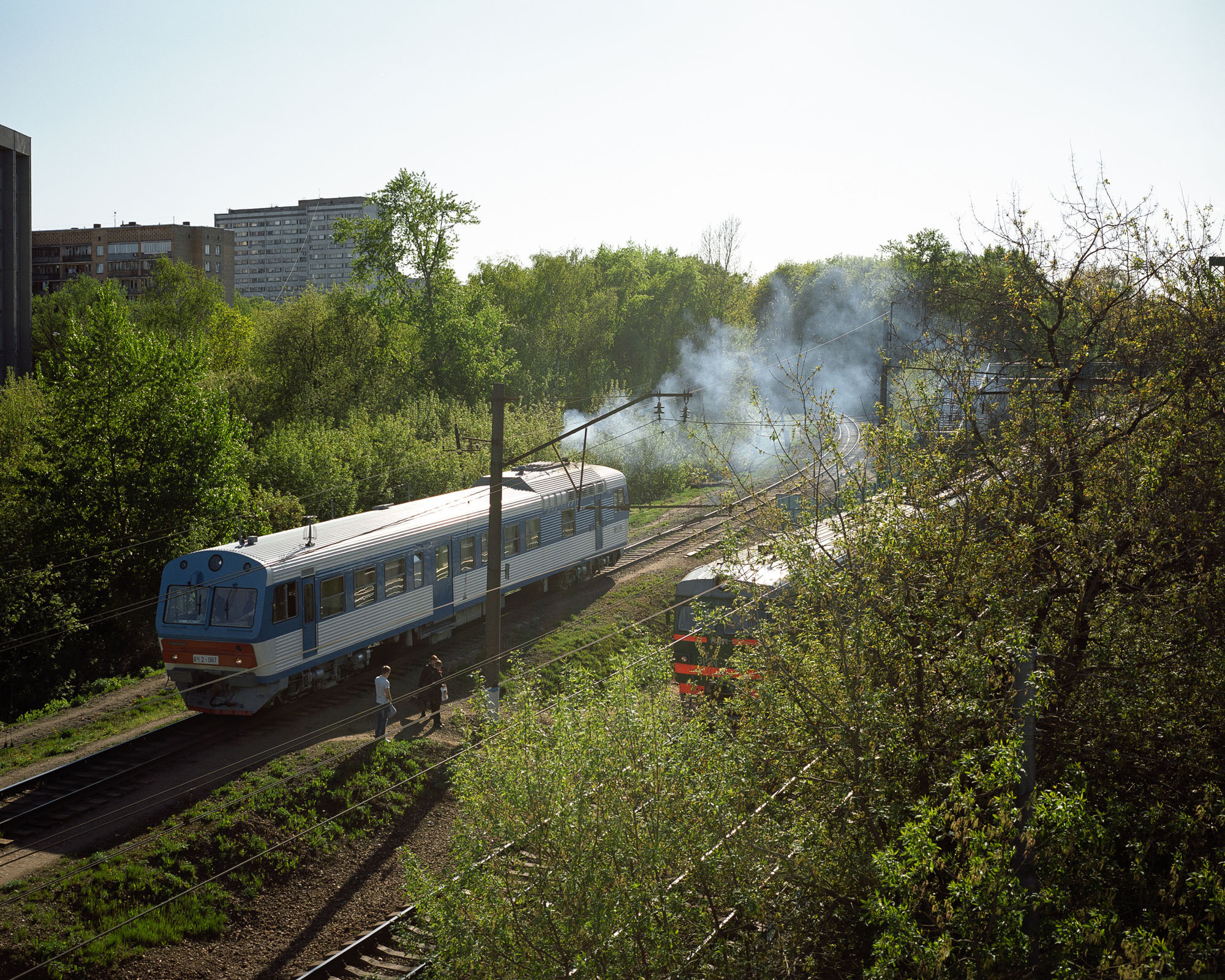 PLATE 41: Residential buildings, railway tracks, commuter train, work train, utility poles c/w power lines, crushed rock, trees, figures of people