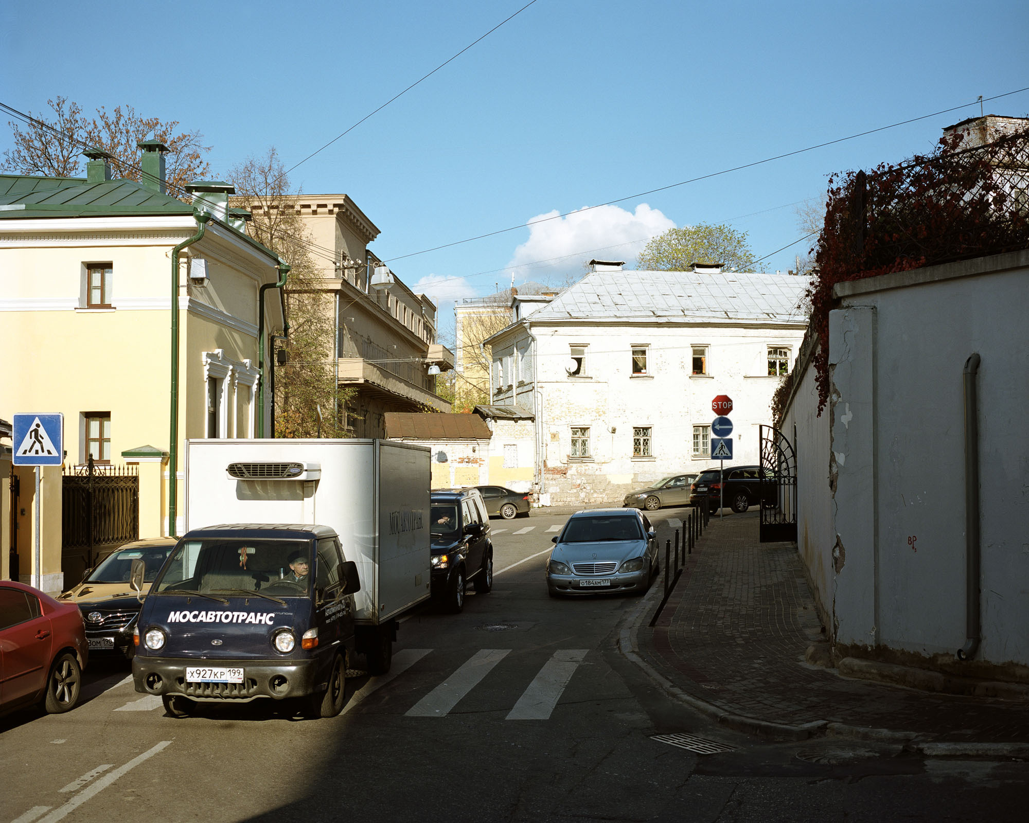 PLATE 28: Historical buildings (incl. replicas; with surveillance cameras, satellite dish), light truck, cars (incl. drivers), plastered wall c/w gate and drain pipe, trees, road signs, pedestrian crossing, street lights