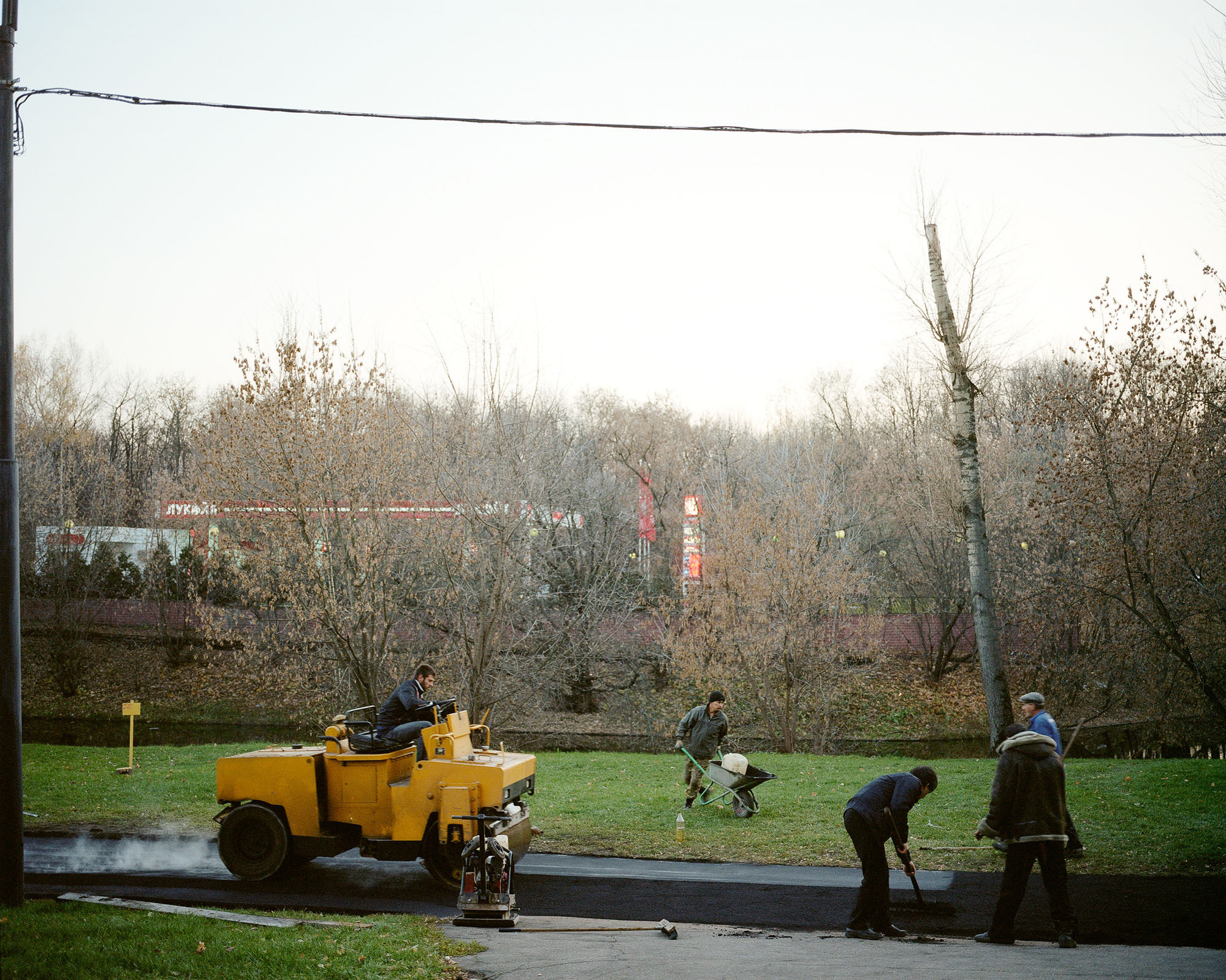 PLATE 55: Figures of workers with tools and equipment, compactor c/w operator, filling station c/w signs, trees, grass, strip of fresh asphalt, power lines