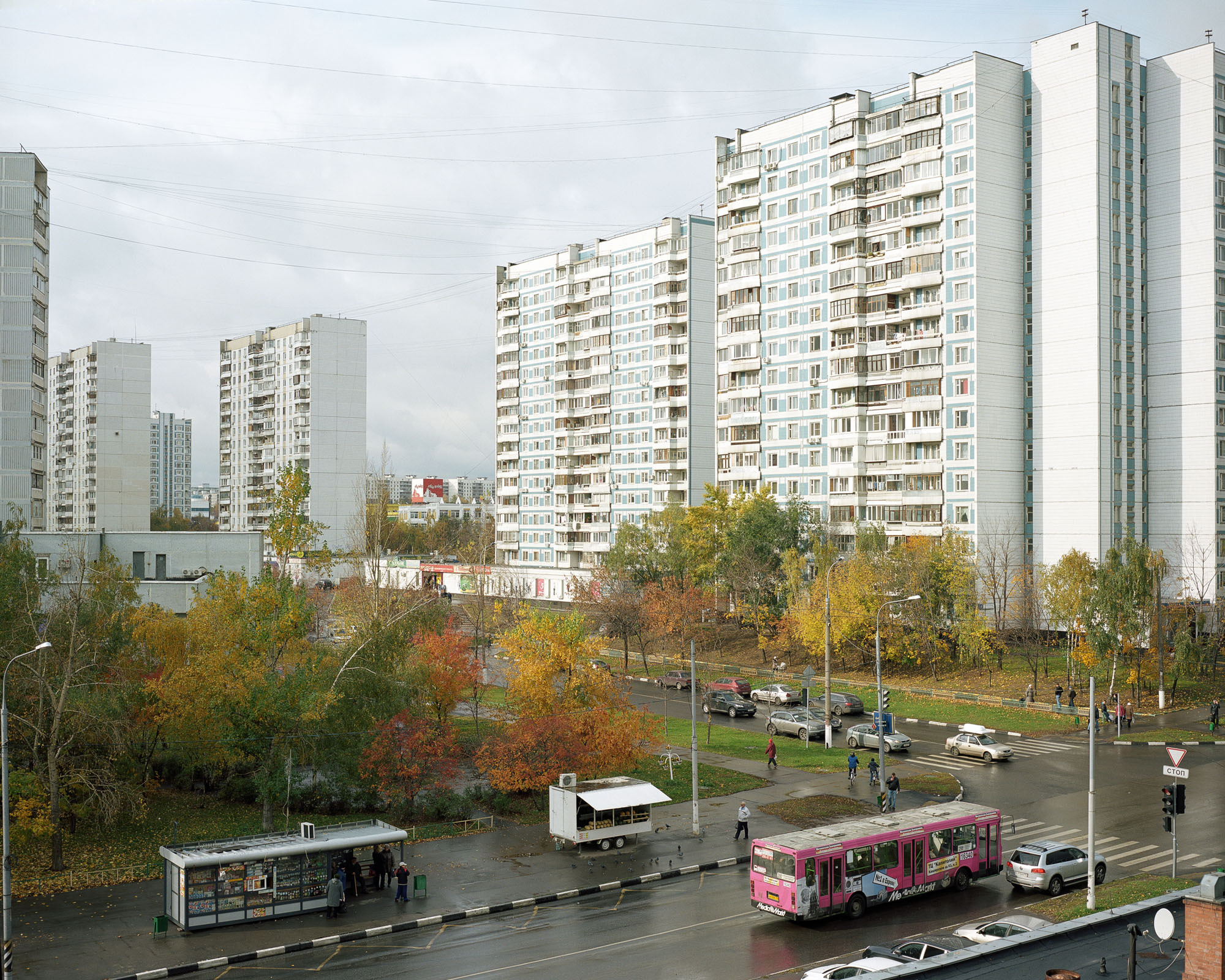 PLATE 44: Residential buildings, 4-way junction with traffic lights and pedestrian crossing, bus stop, mobile and 	semi-permanent kiosks with A/C units (also includes waste bins, flower pots, trees, road signs, lamp posts with power lines, satellite dishes, baby strollers, cars, bus, figures of people)