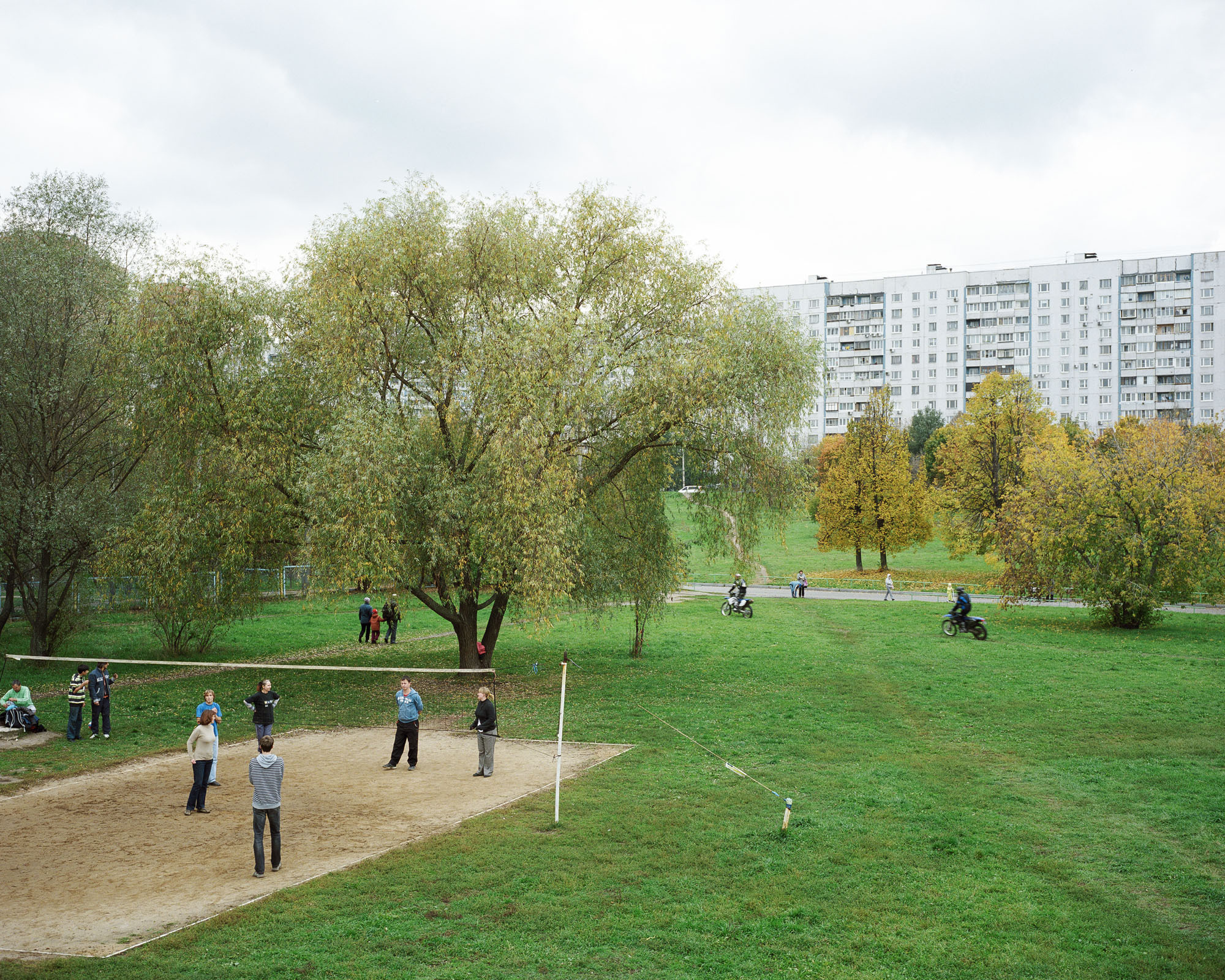 PLATE 50: Residential buildings, volleyball court c/w net, figures of players, trees, grass, paved walkway, A/C units, figures of motorcyclists, figures of people at leisure, barriers