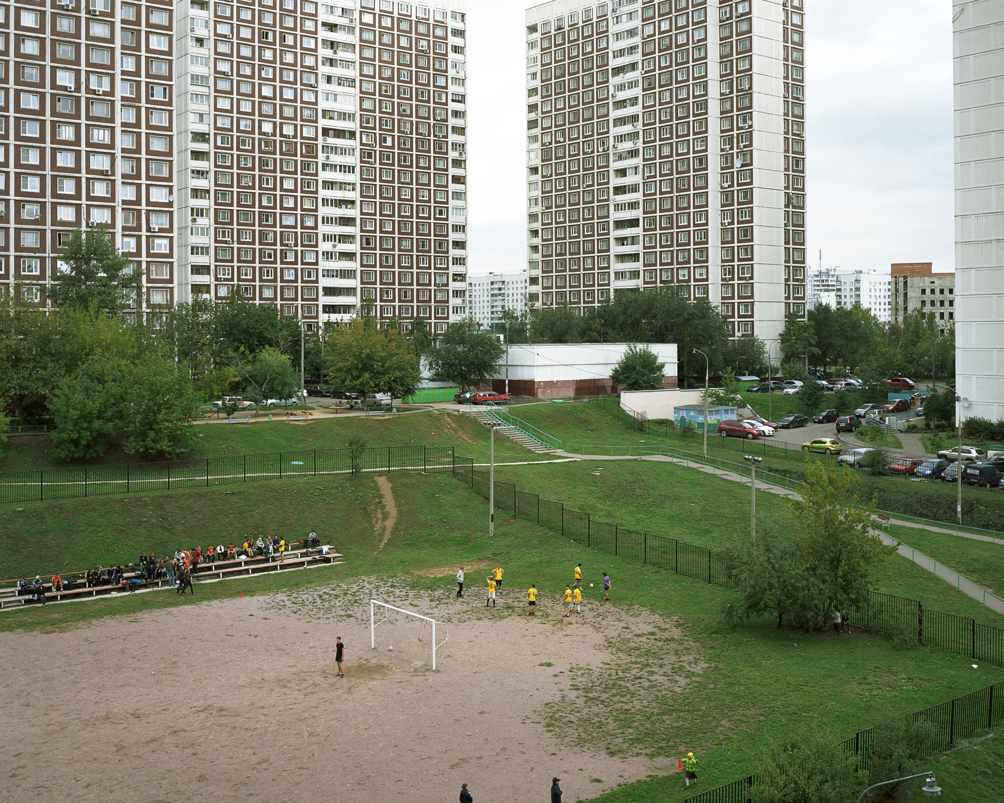 PLATE 9: Residential buildings, assorted small buildings, football field with figures of players and supporters, metal fence (also includes lighting posts and power lines, cars, paved walkways with stairs and handrails, benches, trees, A/C units, satellite dishes)
