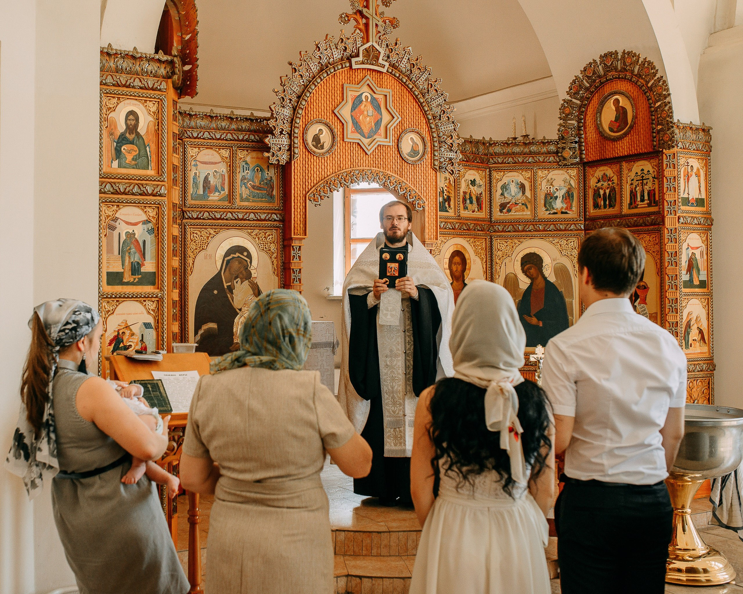 Молитва в православном храме: священник читает Священное Писание перед семьей во время обряда крещения.