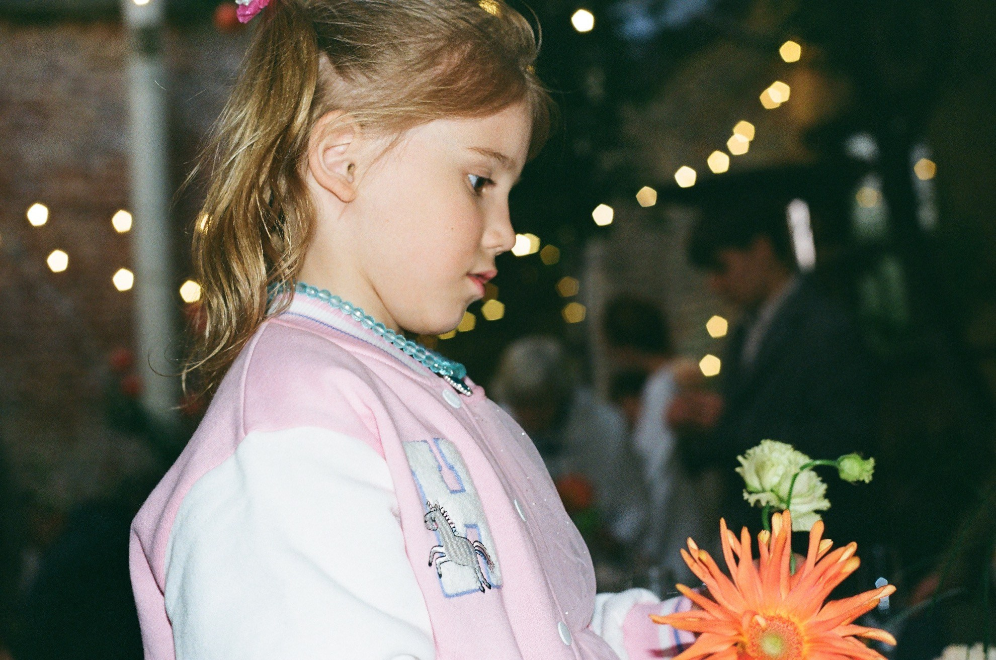 Юная гостья держит оранжевый георгин среди гирлянд огоньков, плёнка Kodak Gold 200