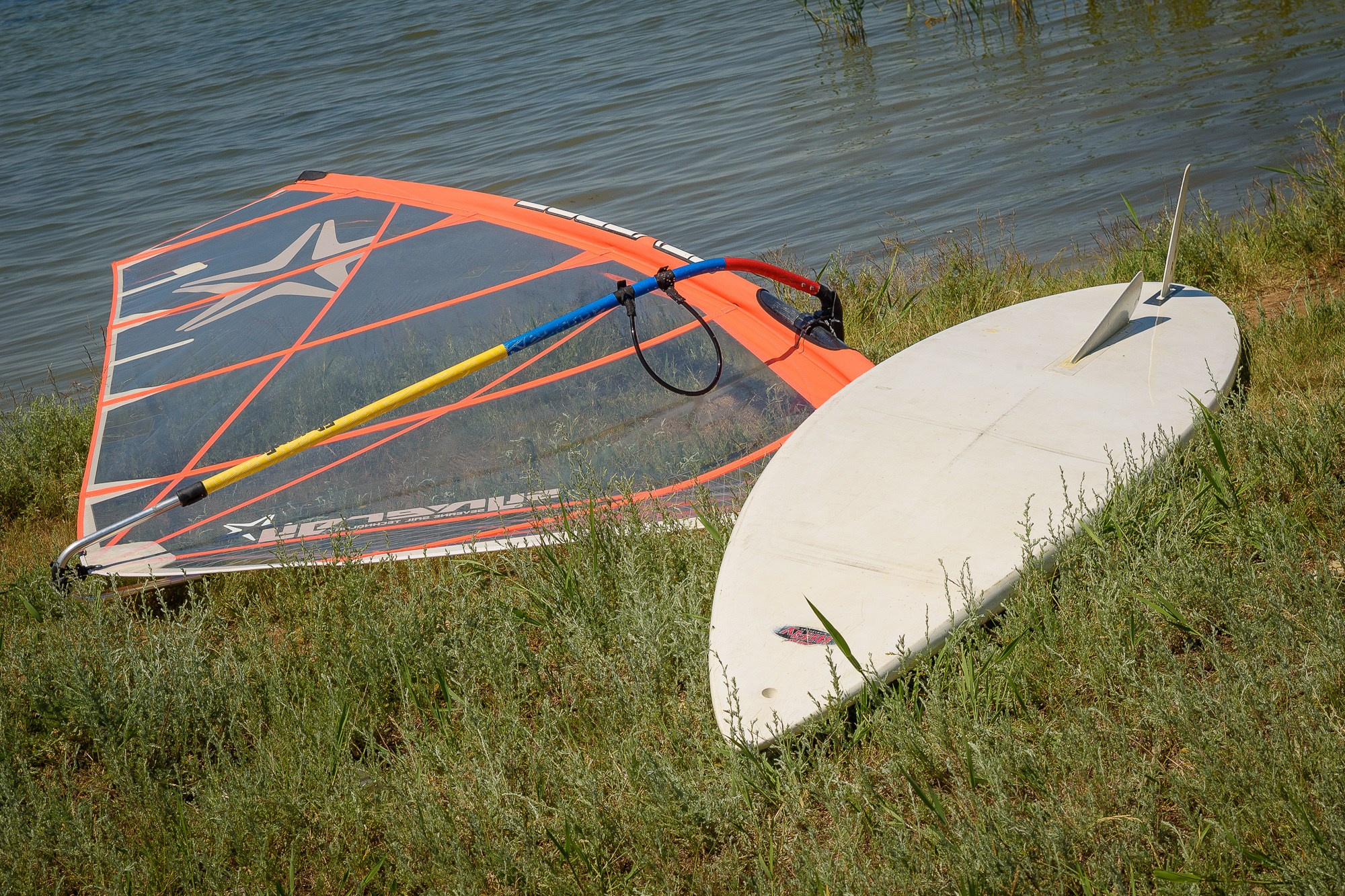 Виндсёрф лежит на траве у кромки воды