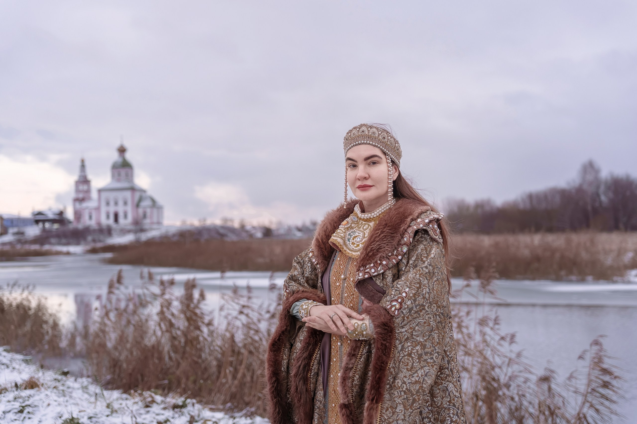 A girl in a boyar costume on the background of a temple in Suzdal by the river