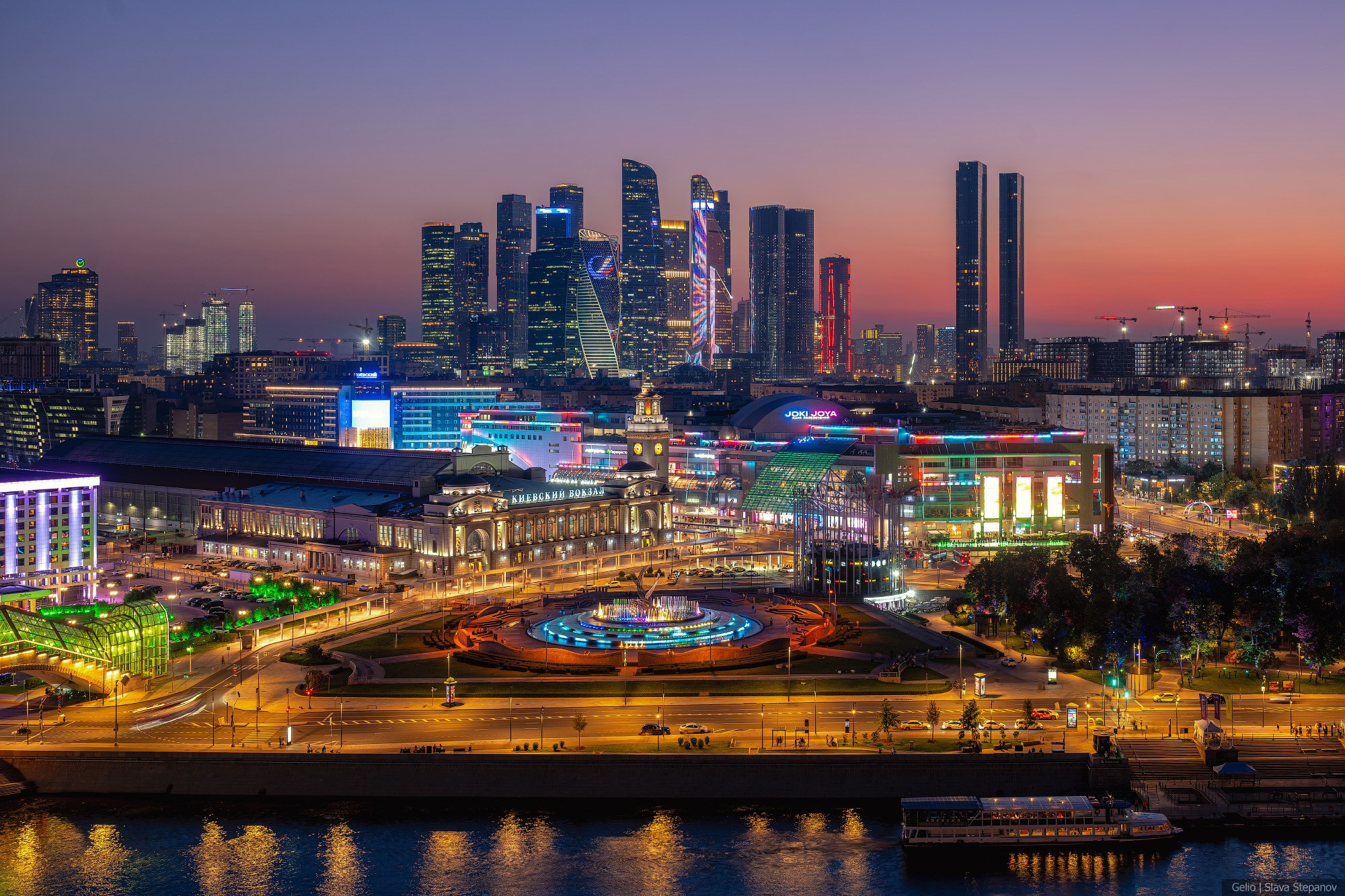 Large-scale evening panorama of Moscow at sunset. Historical Kiyevsky railway station in the foreground and modern illuminated skyscrapers of the Moscow-City complex in the background. Gelio.