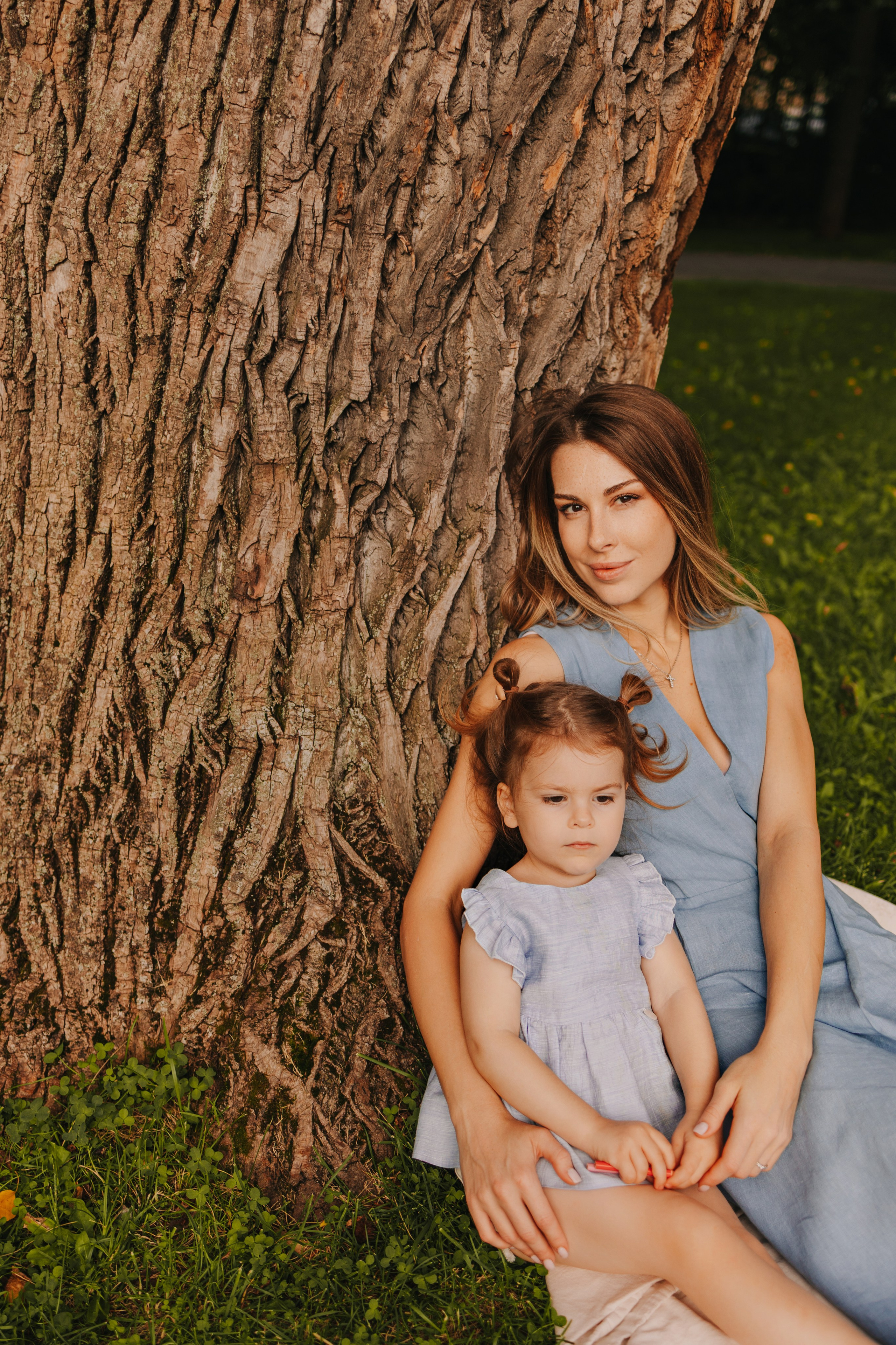 Мама обнимает дочку возле большого дерева, семейное фото