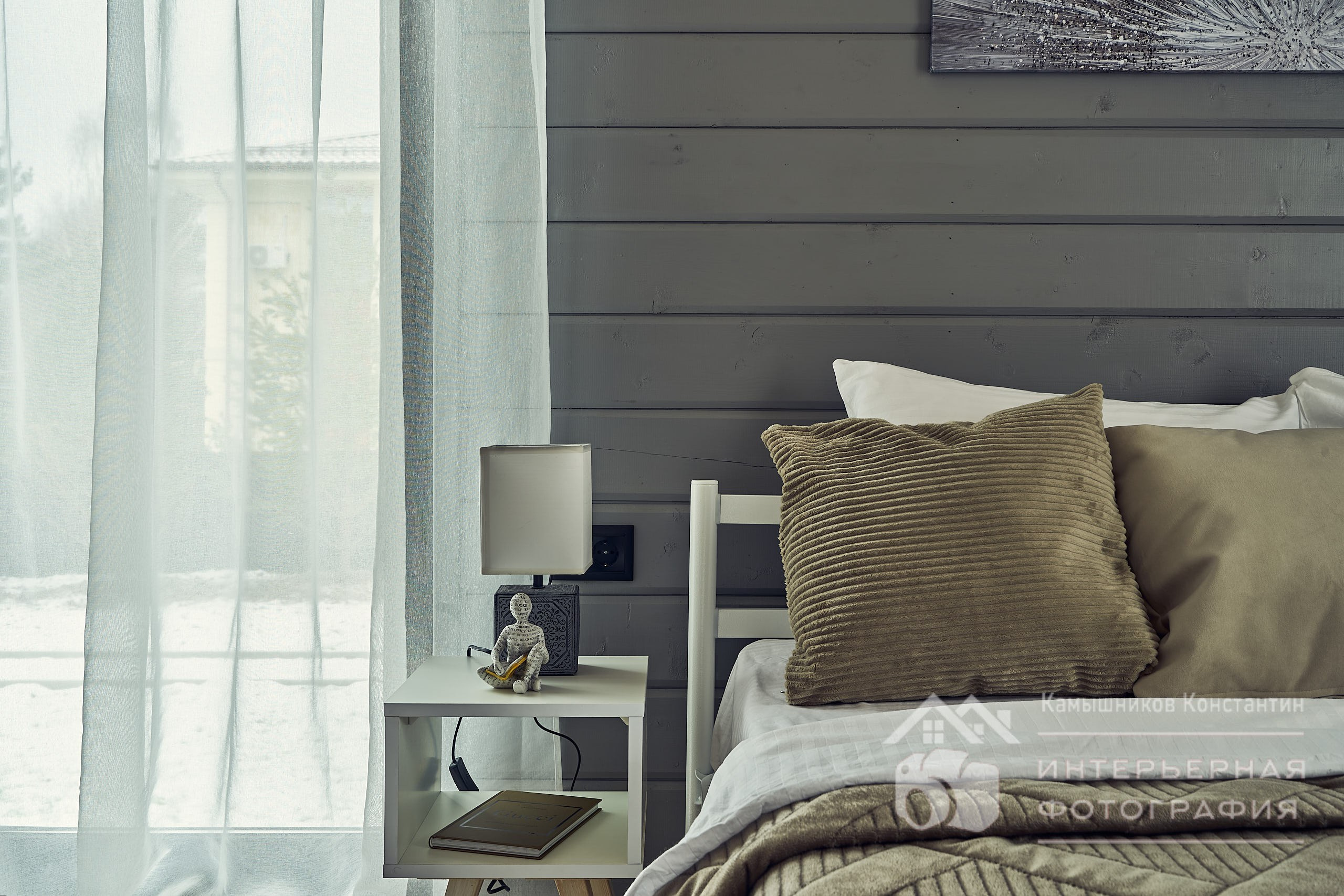 Интерьерное фото с подушками, прикроватным столиком и светильником на нем, а также части панорамного окна в загородном доме в Подмосковье