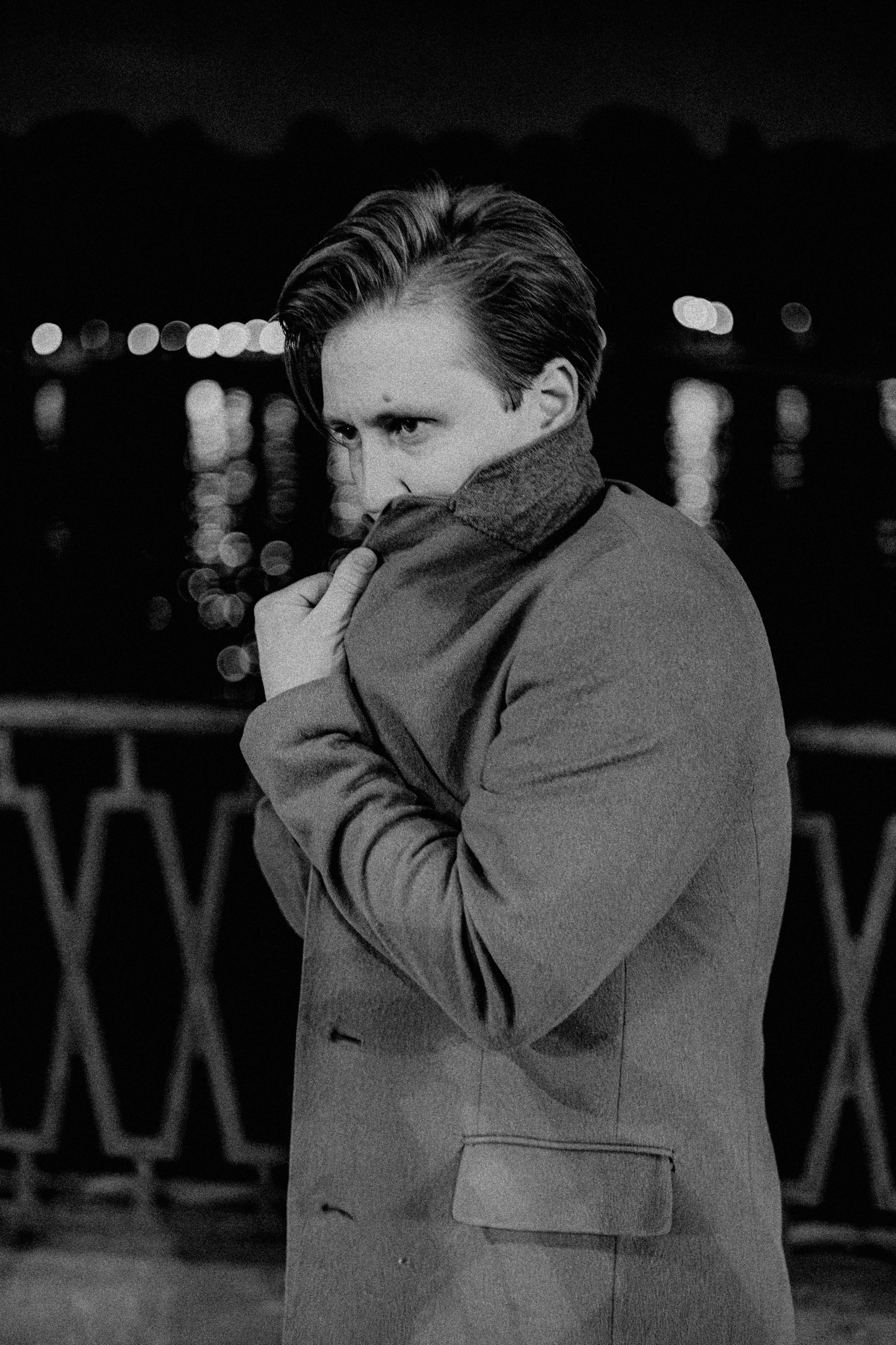 Молодой человек, поэт укутывается в пальто на набережной.