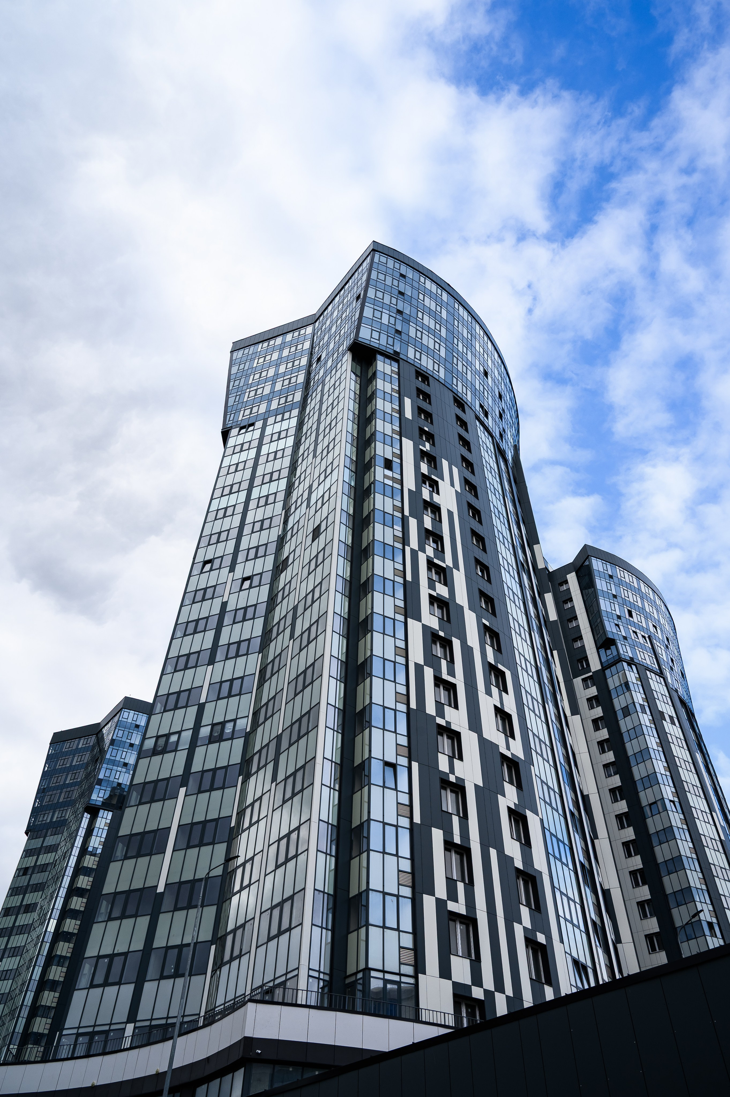 Фасад жилого комплекса Авалон-Сити на фоне неба с облаками, отражения и контраст материалов