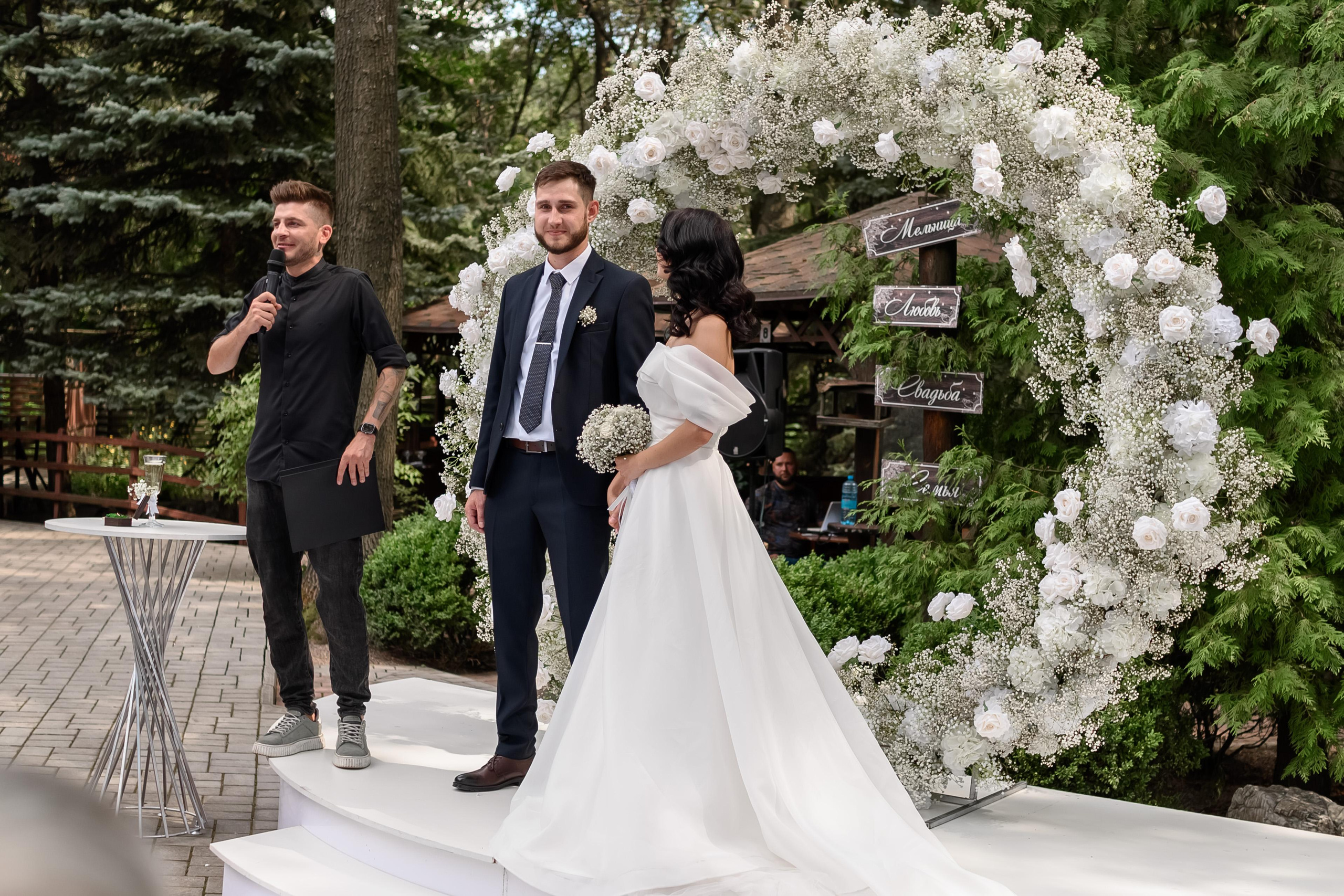 Свадебная речь возле арки из белых цветов