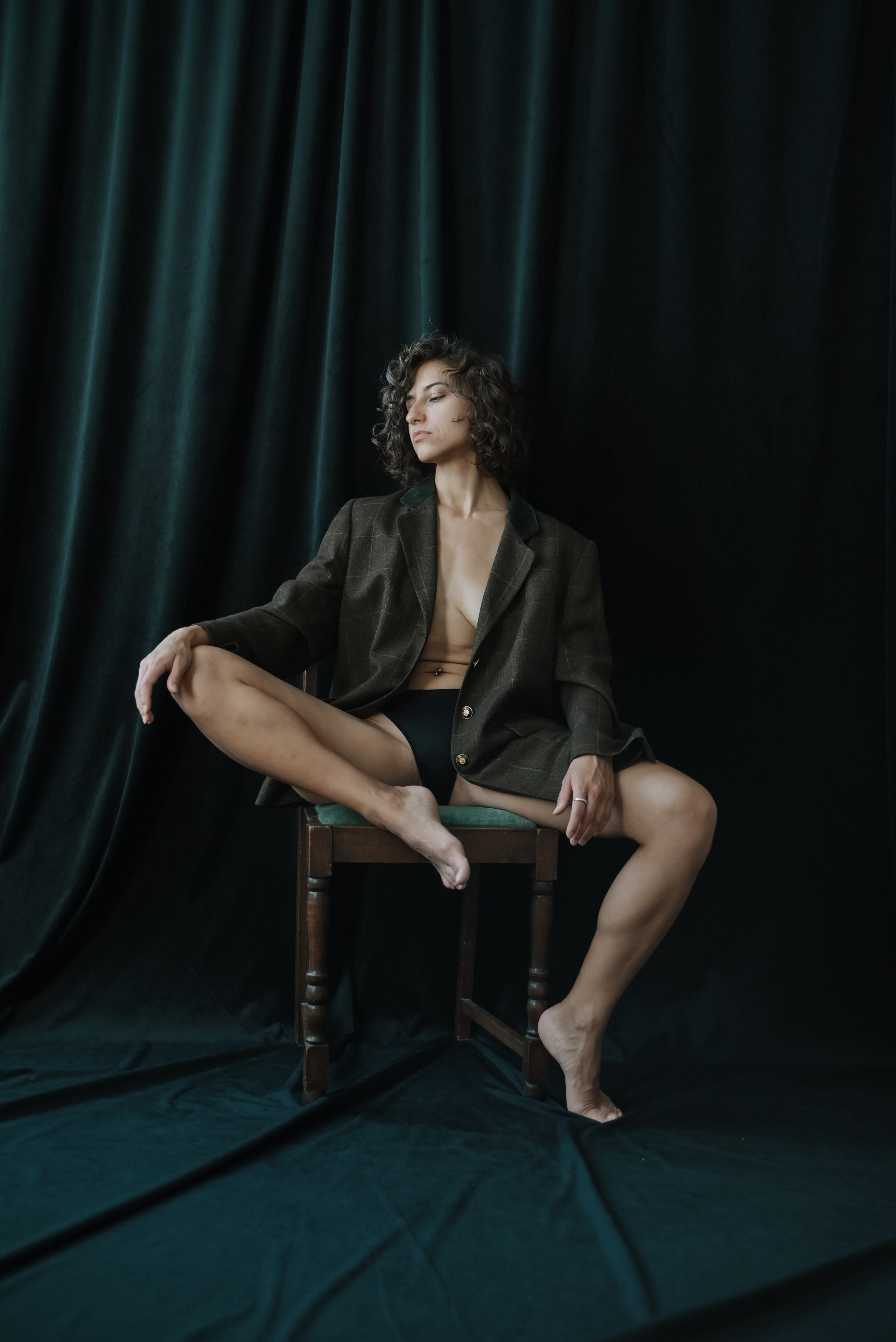 Boudoir photoshoot — woman in black bodysuit on chair, confident pose, dramatic studio light