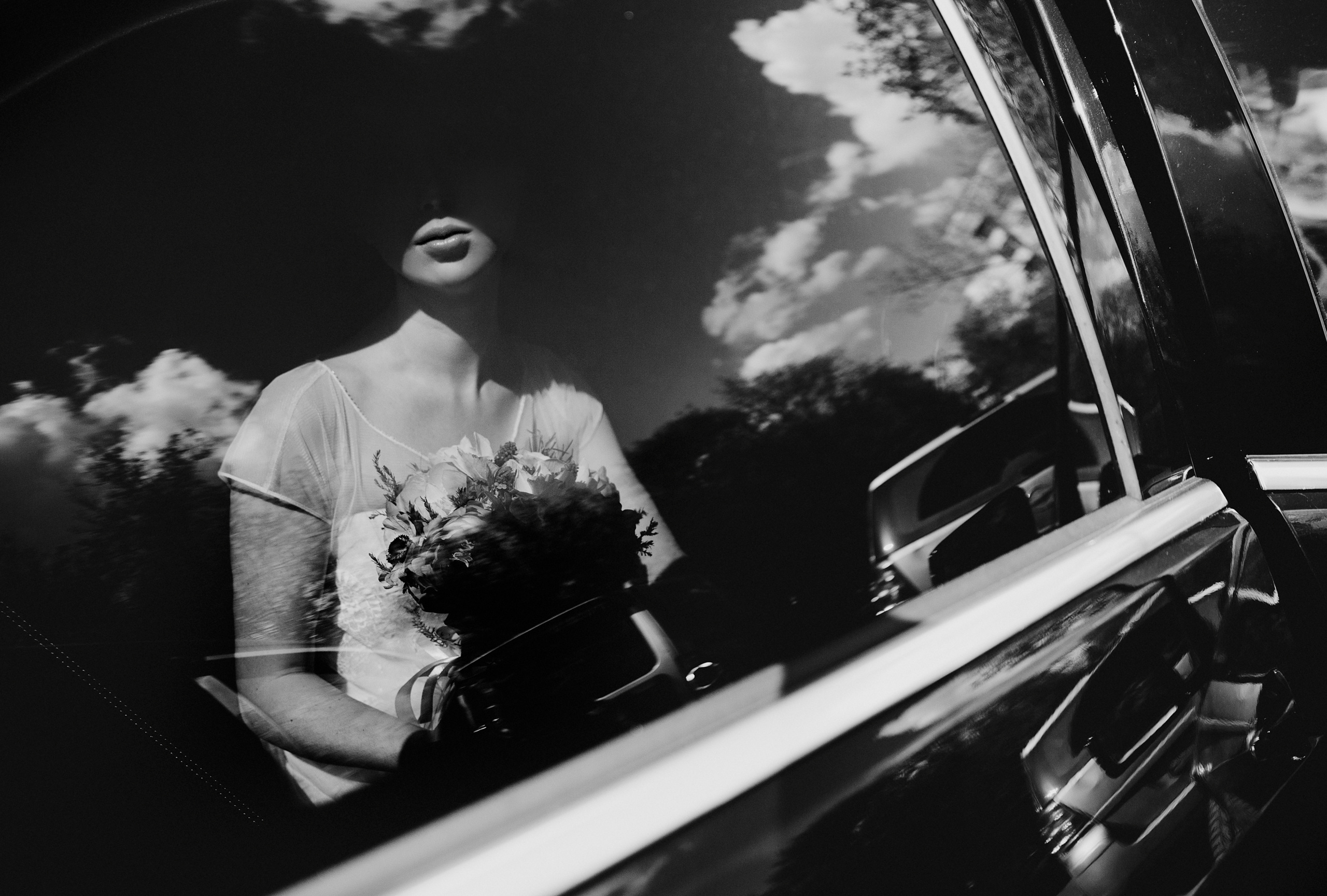Невеста сидит в черном автомобиле и солнце светит на ее губы